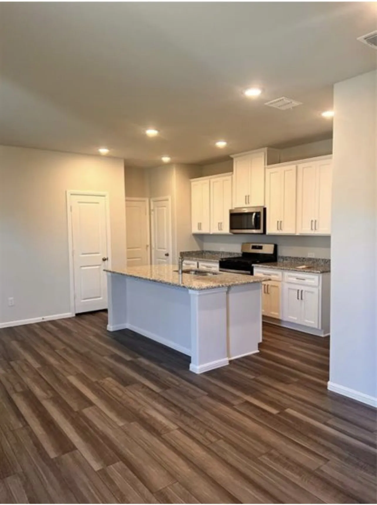 Kitchen featuring a central island with a light-toned countertop, white cabinetry with silver-toned hardware, stainless steel microwave, black range, and wood-finish flooring