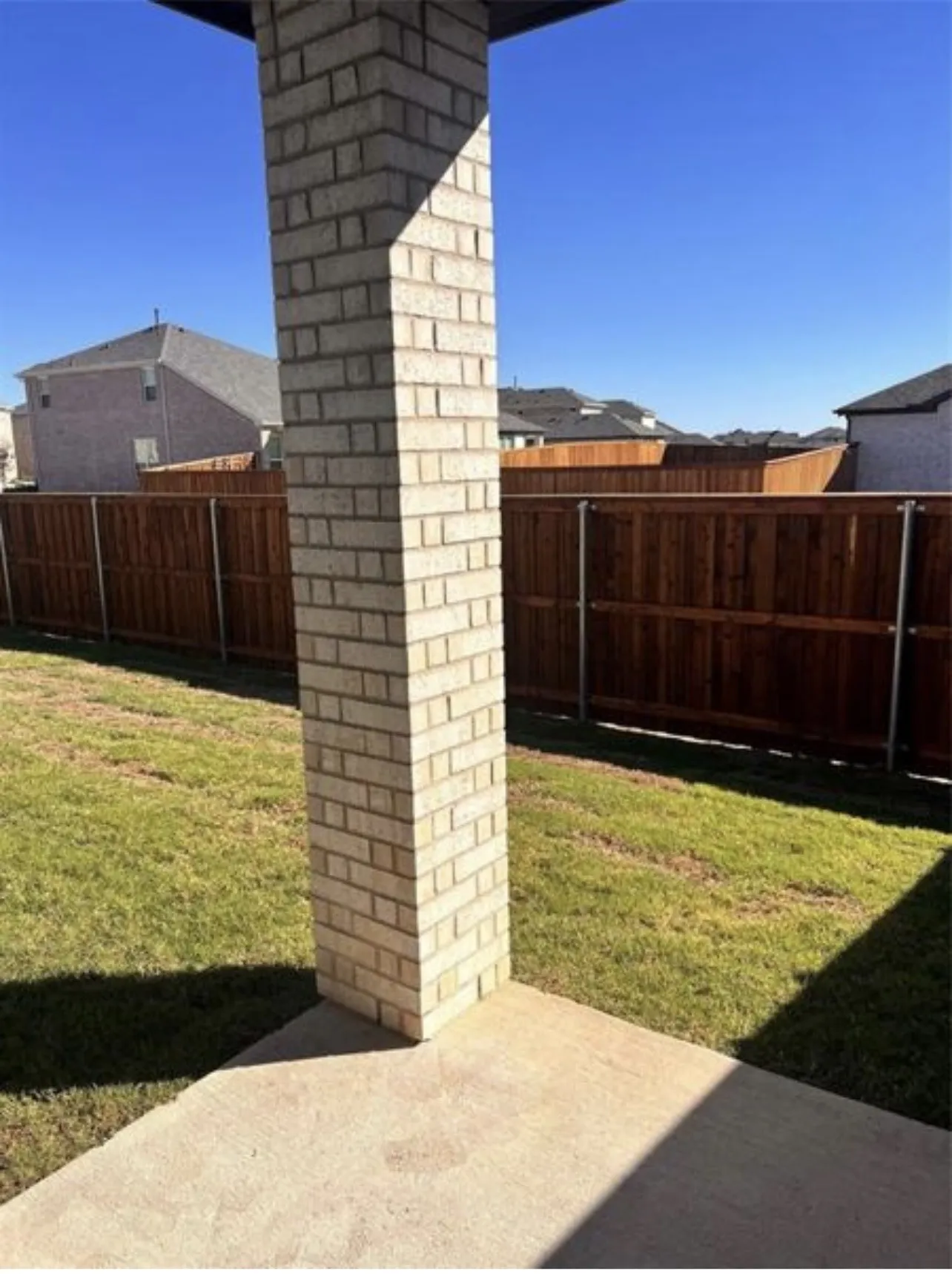 Expansive backyard featuring a concrete patio, a light-colored brick column, a manicured lawn, and a tall wooden privacy fence