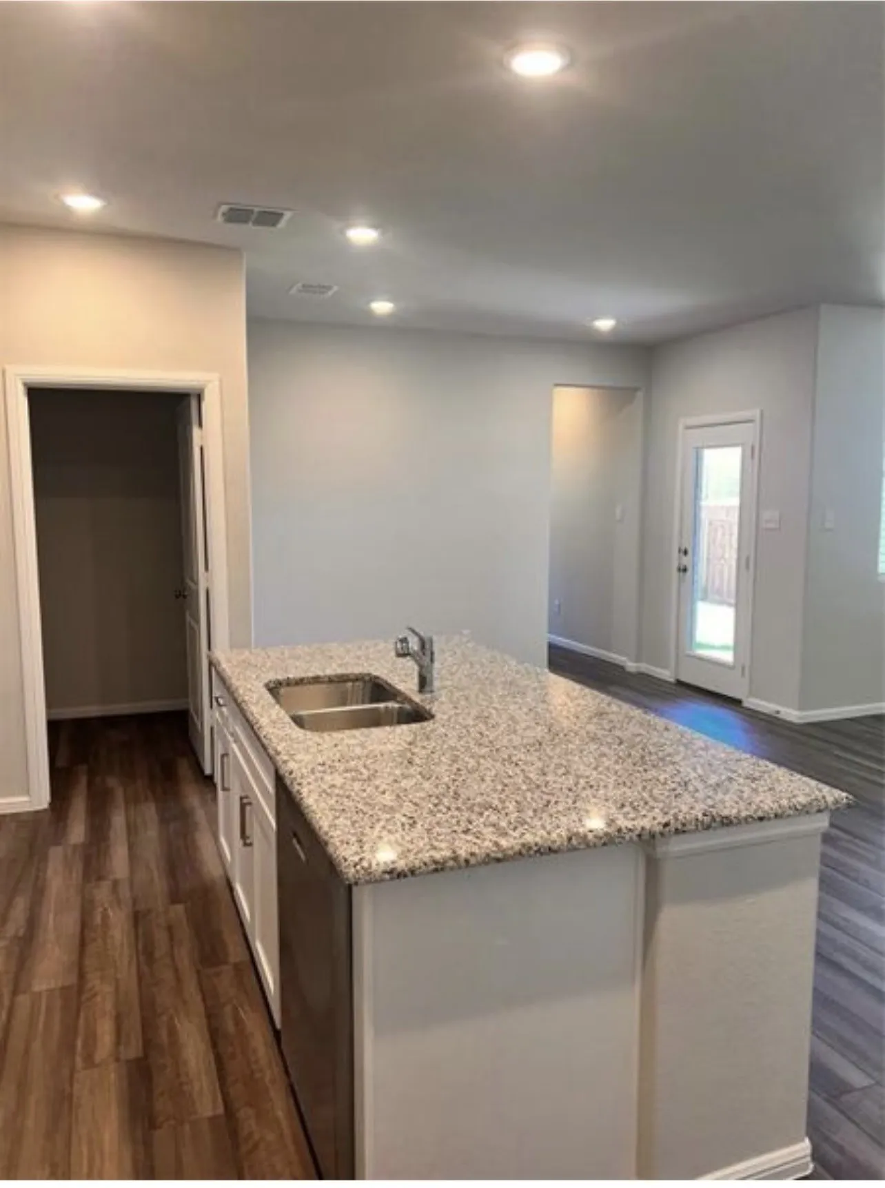 Kitchen island featuring a double basin stainless steel sink, granite countertop, and white cabinetry