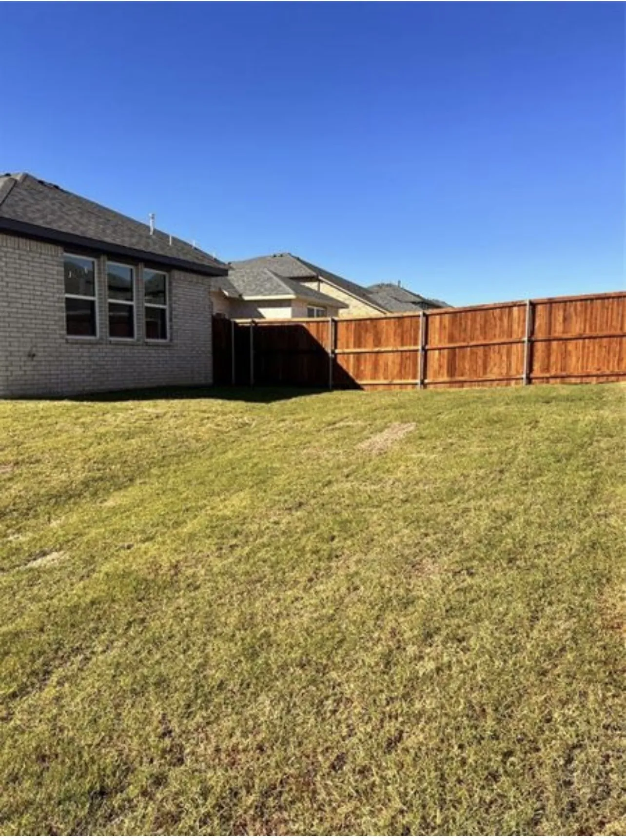 Expansive backyard featuring a new wood privacy fence, a brick exterior, and multiple windows