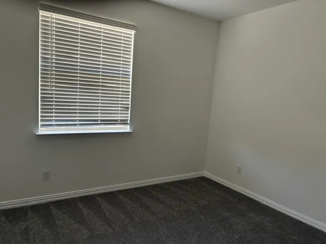 Room featuring light gray walls, dark gray carpet, white baseboards, and a window with white blinds