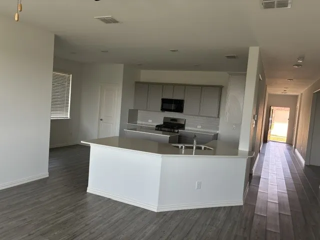 Open-concept kitchen featuring an island with a built-in sink, light gray cabinetry, a tile backsplash, and stainless steel appliances