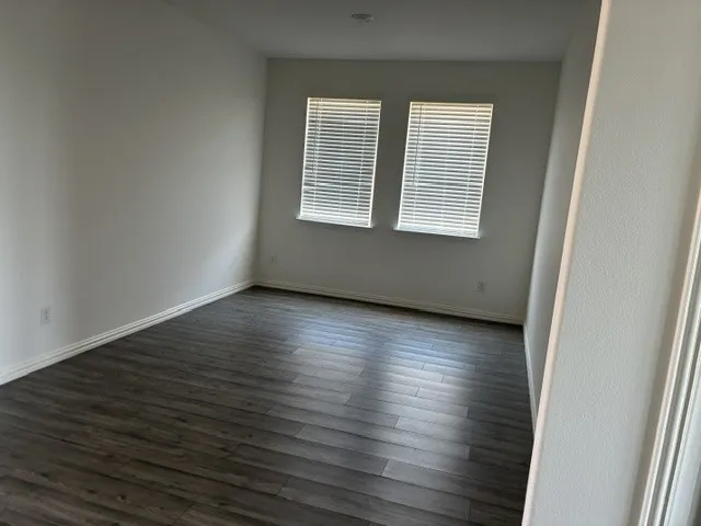 Room featuring two windows with blinds, wood-finish flooring, white baseboards, and neutral wall tones
