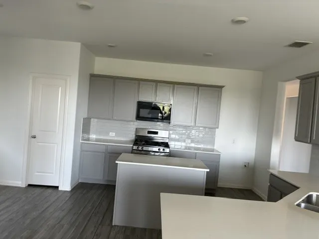Kitchen featuring gray shaker-style cabinetry, stainless steel gas range, subway tile backsplash, and light-toned countertops