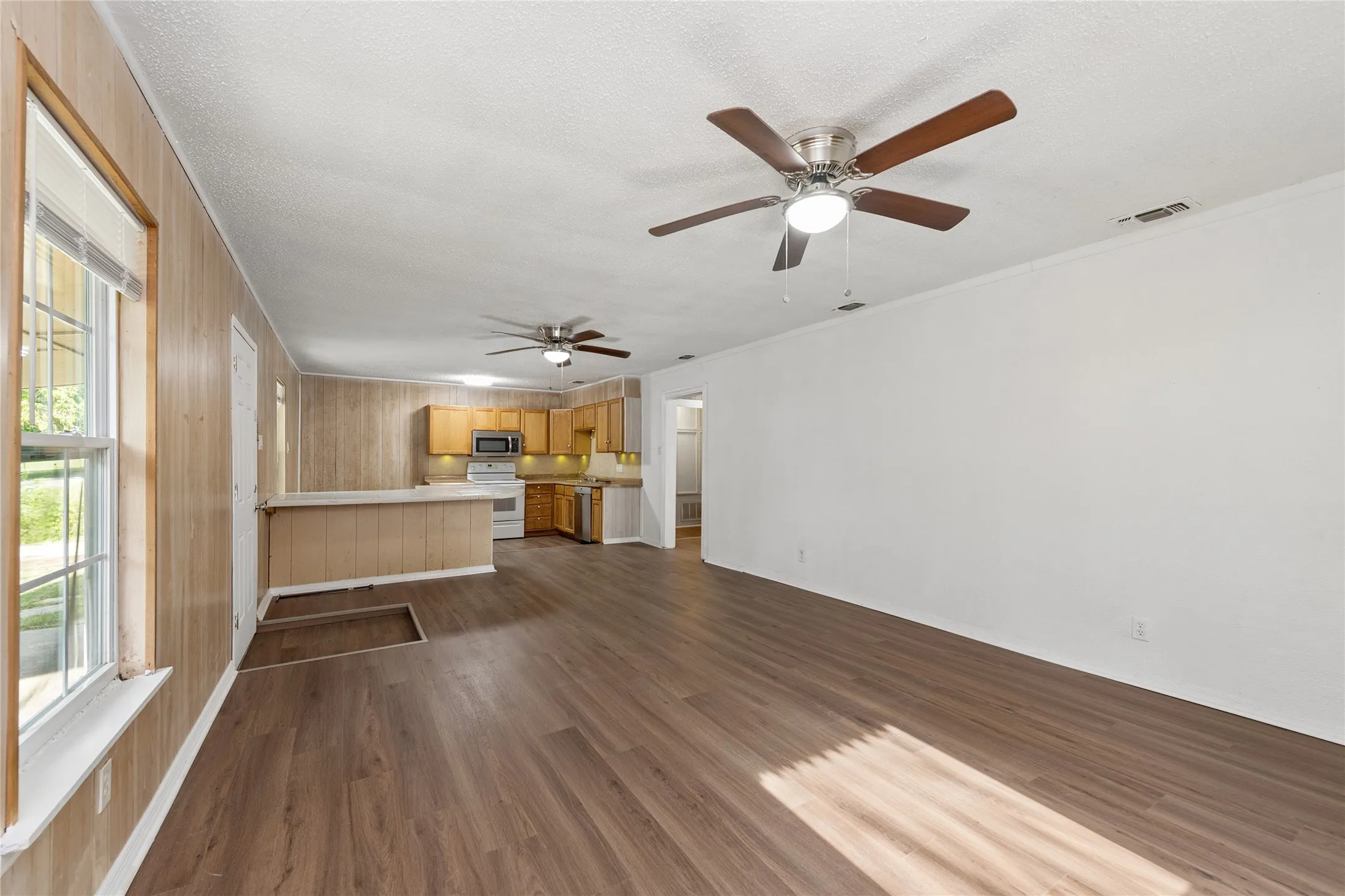 Open-concept living space featuring wood-finish flooring, two ceiling fans, and a kitchen with wood cabinetry and stainless steel appliances