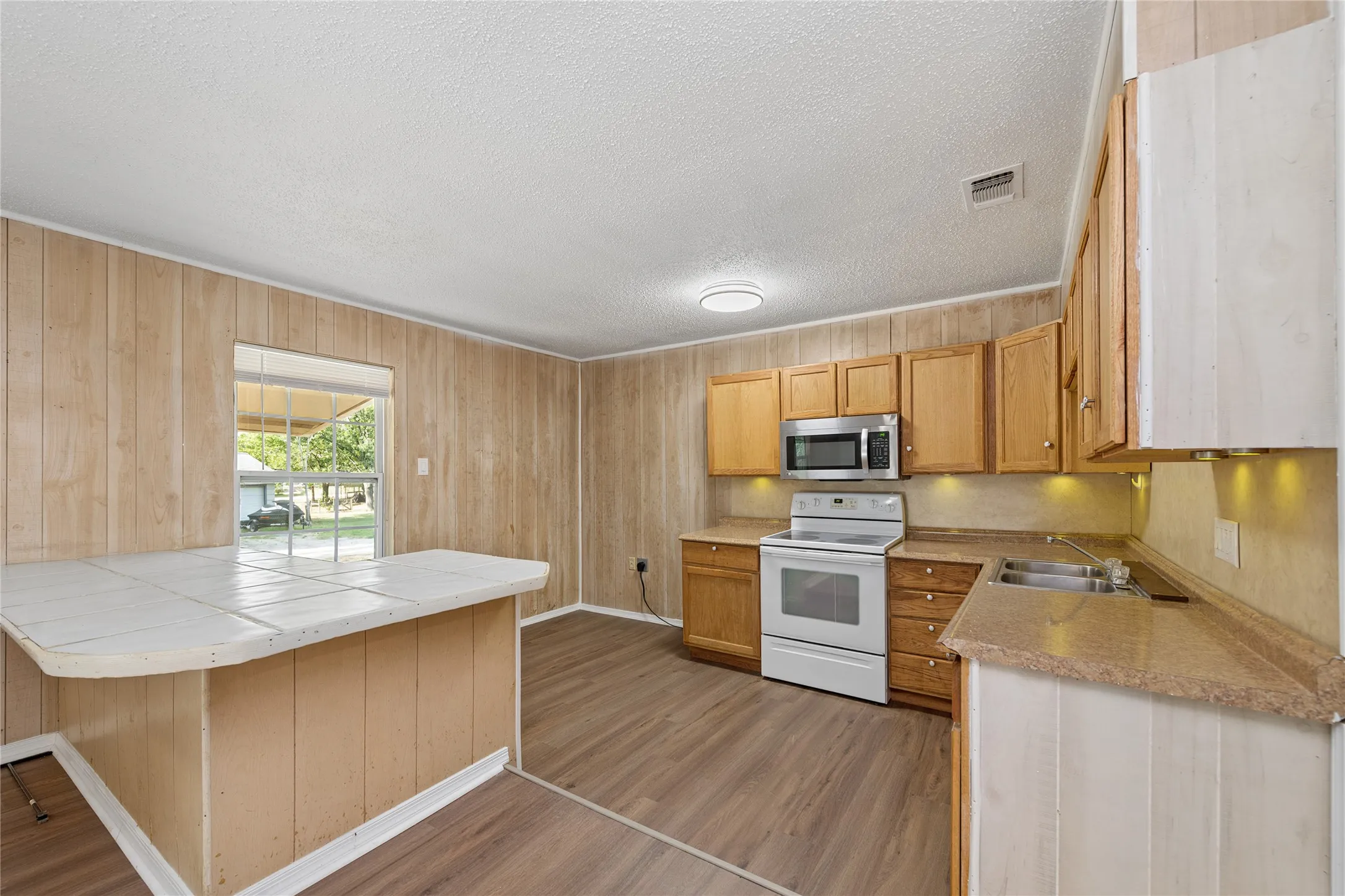 U-shaped kitchen with wood-finish flooring, wood cabinetry, stainless steel microwave, white electric range, and laminate countertops