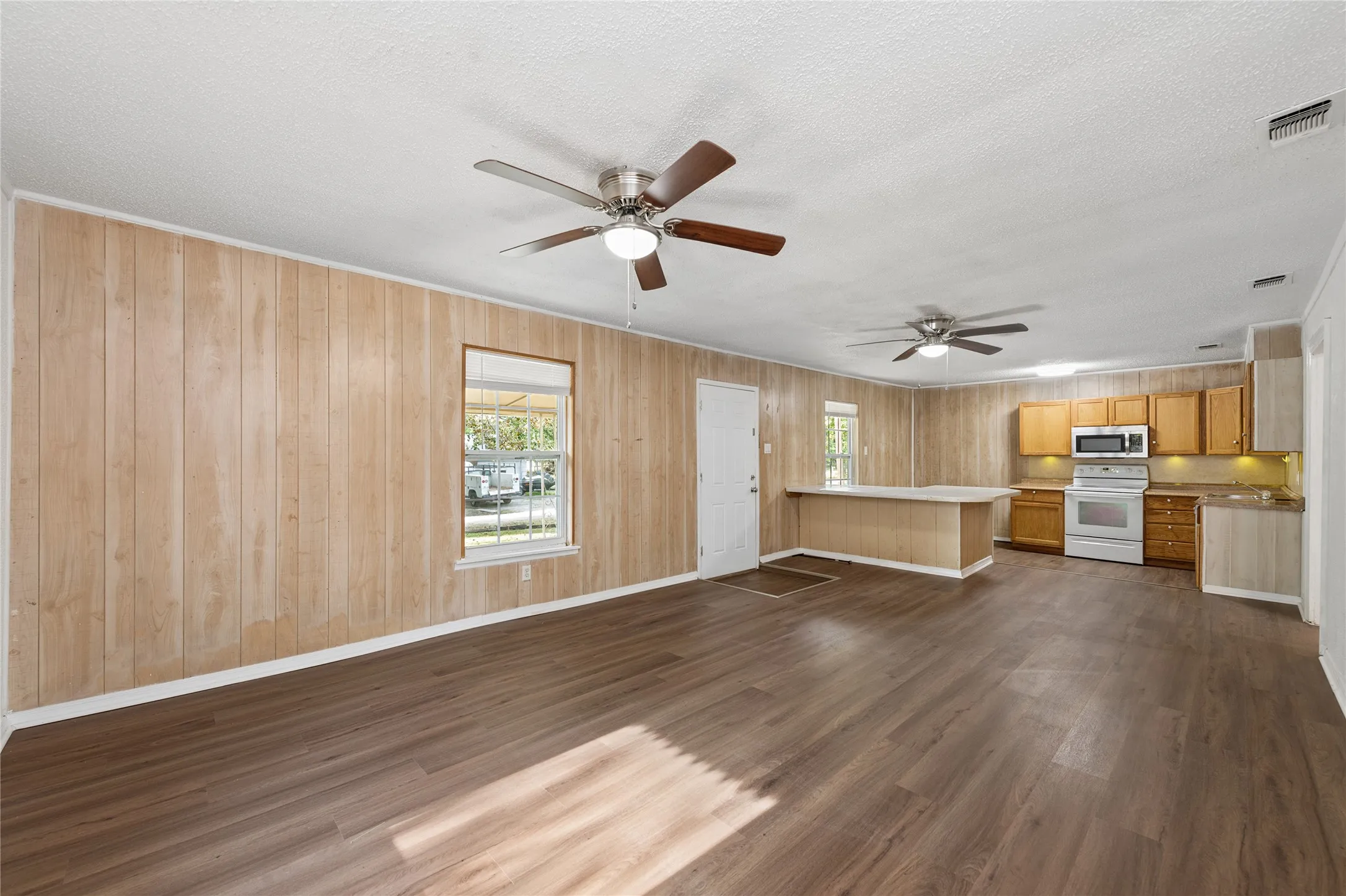 Open-concept living space featuring wood-finish flooring, paneled walls, and two ceiling fans
