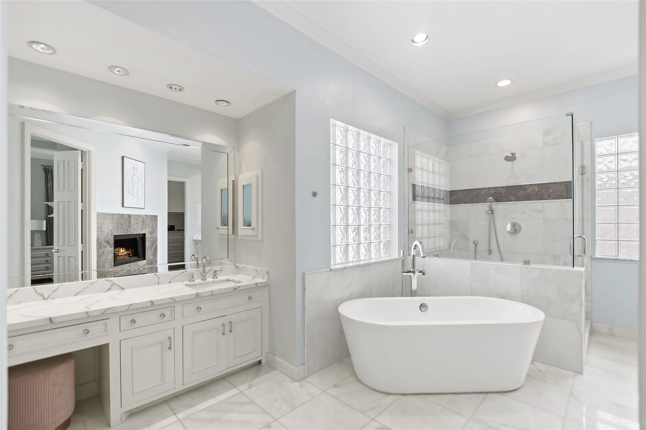 Spacious bathroom featuring a freestanding soaking tub, a large glass-enclosed shower, dual vanity with a white marble-finish countertop, white cabinetry, and recessed lighting
