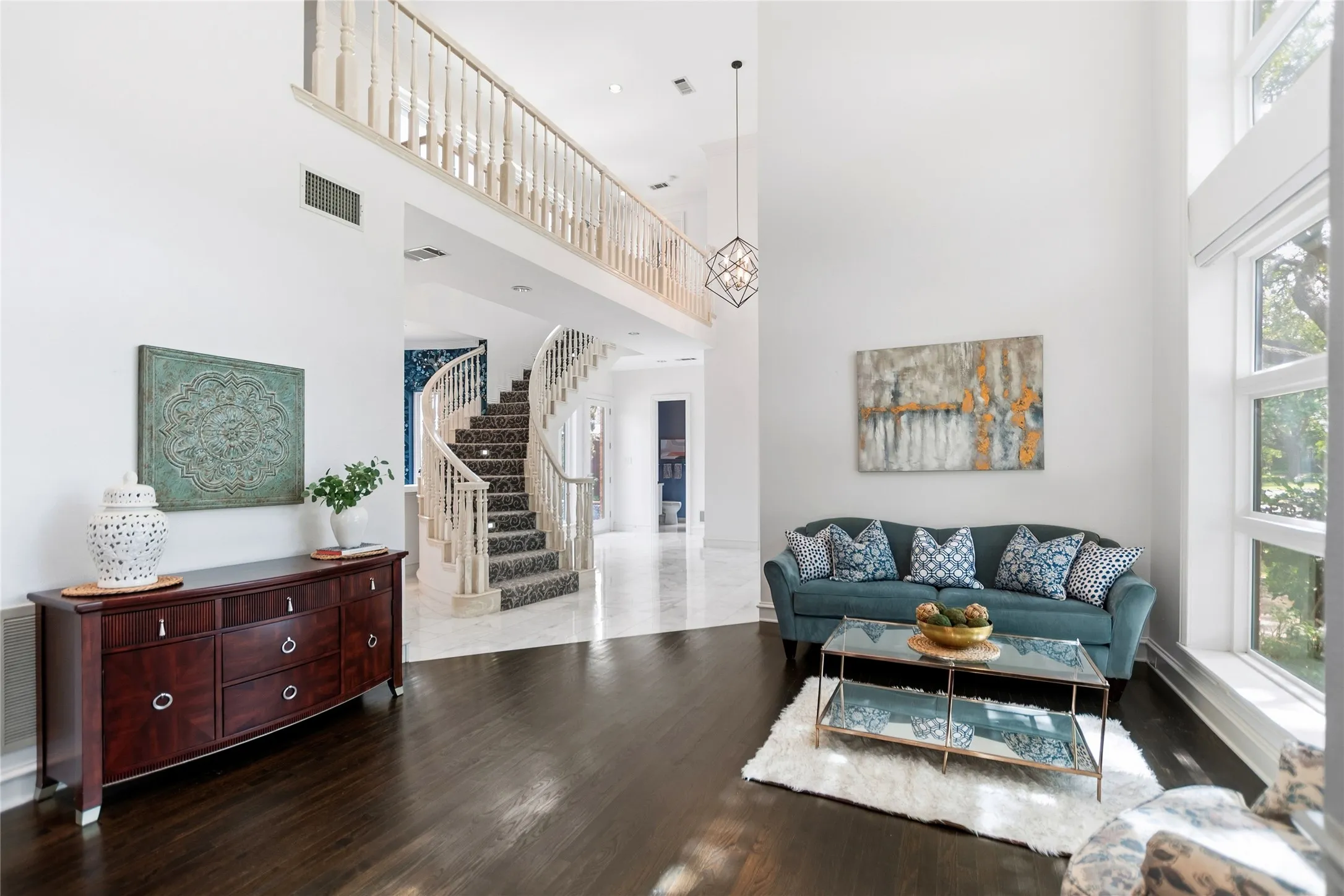 Grand two-story entry featuring dark wood-finish flooring, a spiral staircase with intricate balusters, a second-story landing with matching railing, expansive windows, and a geometric chandelier