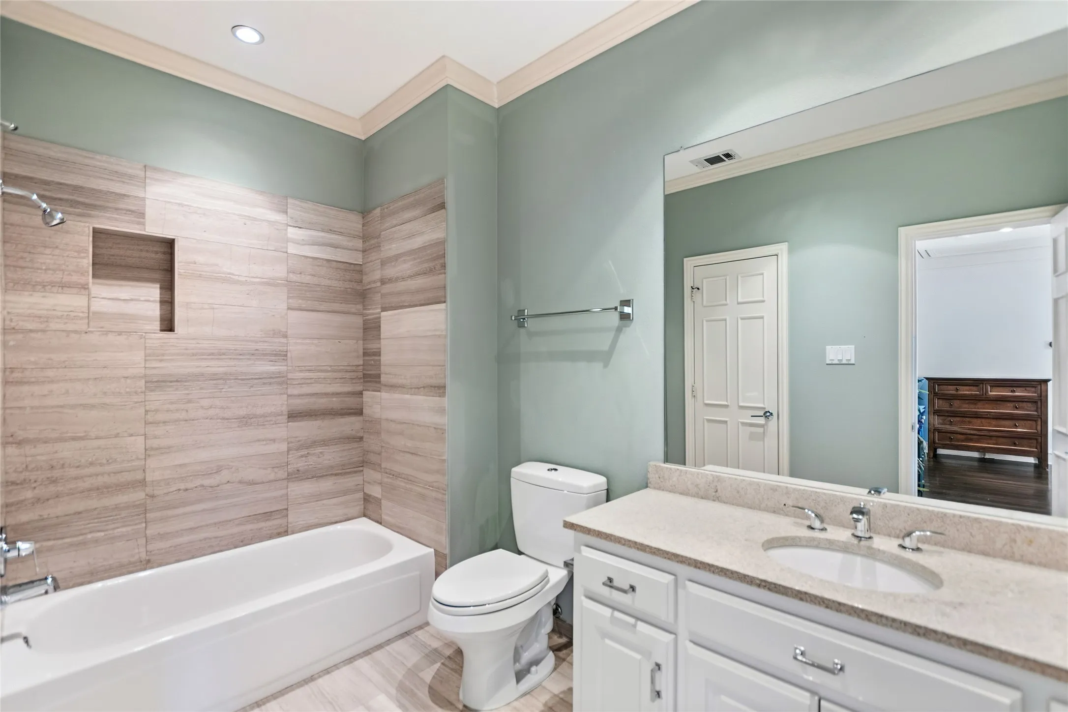 Bathroom featuring a built-in tub with a tiled surround, a recessed shower niche, a single vanity with an integrated sink, and a light-toned countertop