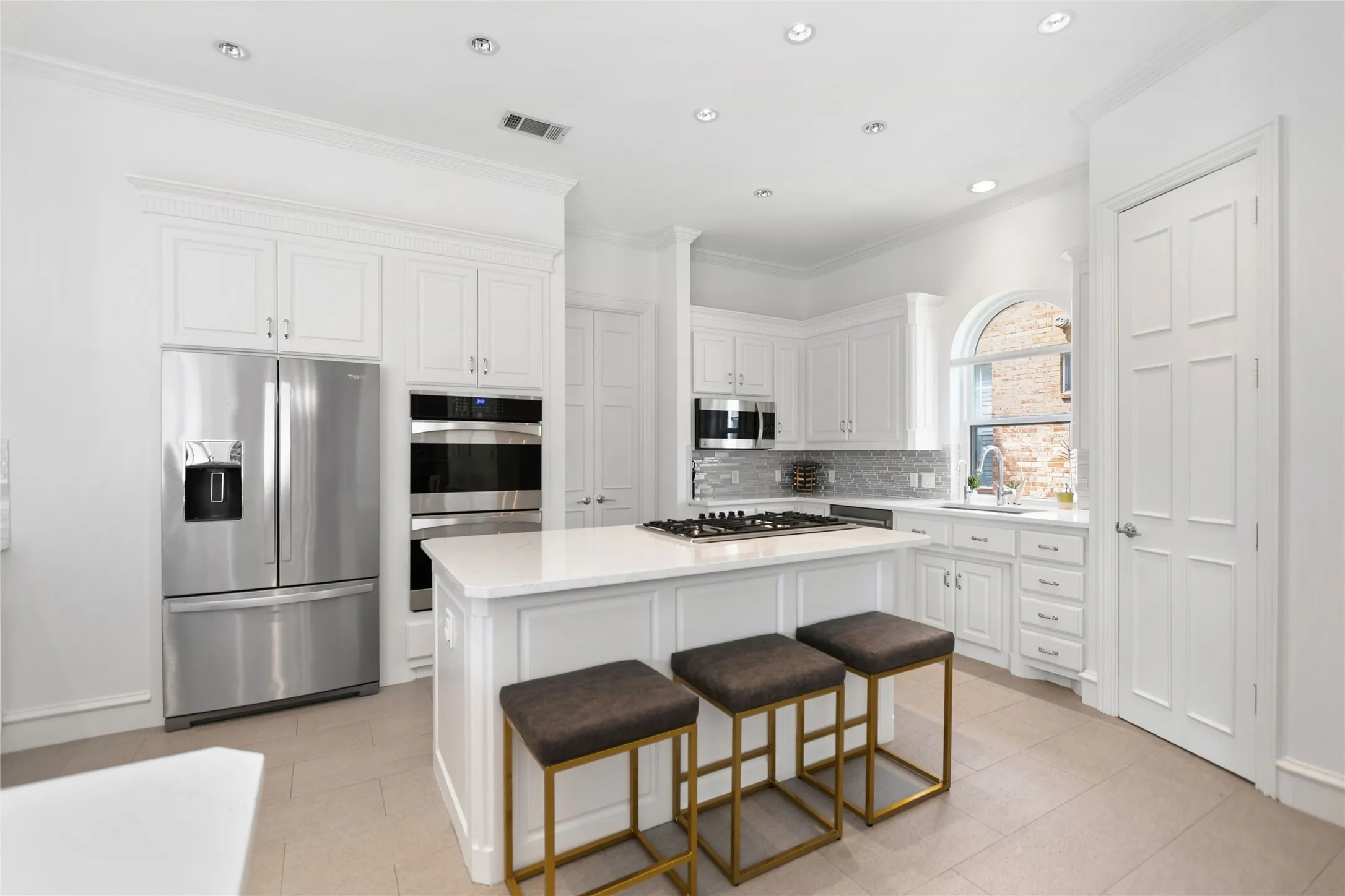 Contemporary kitchen featuring white cabinetry, stainless steel appliances, a center island with a gas cooktop, a tile backsplash, and an arched window above the sink