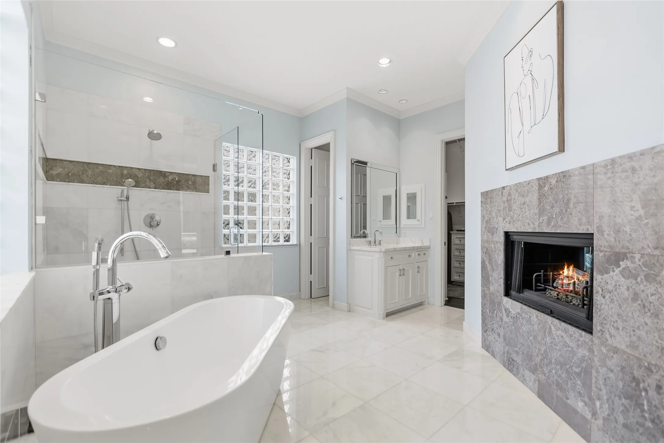 Bathroom featuring a freestanding soaking tub, a tiled walk-in shower with glass enclosure, a fireplace with a stone surround, marble-finish flooring, and a single vanity with a white cabinet
