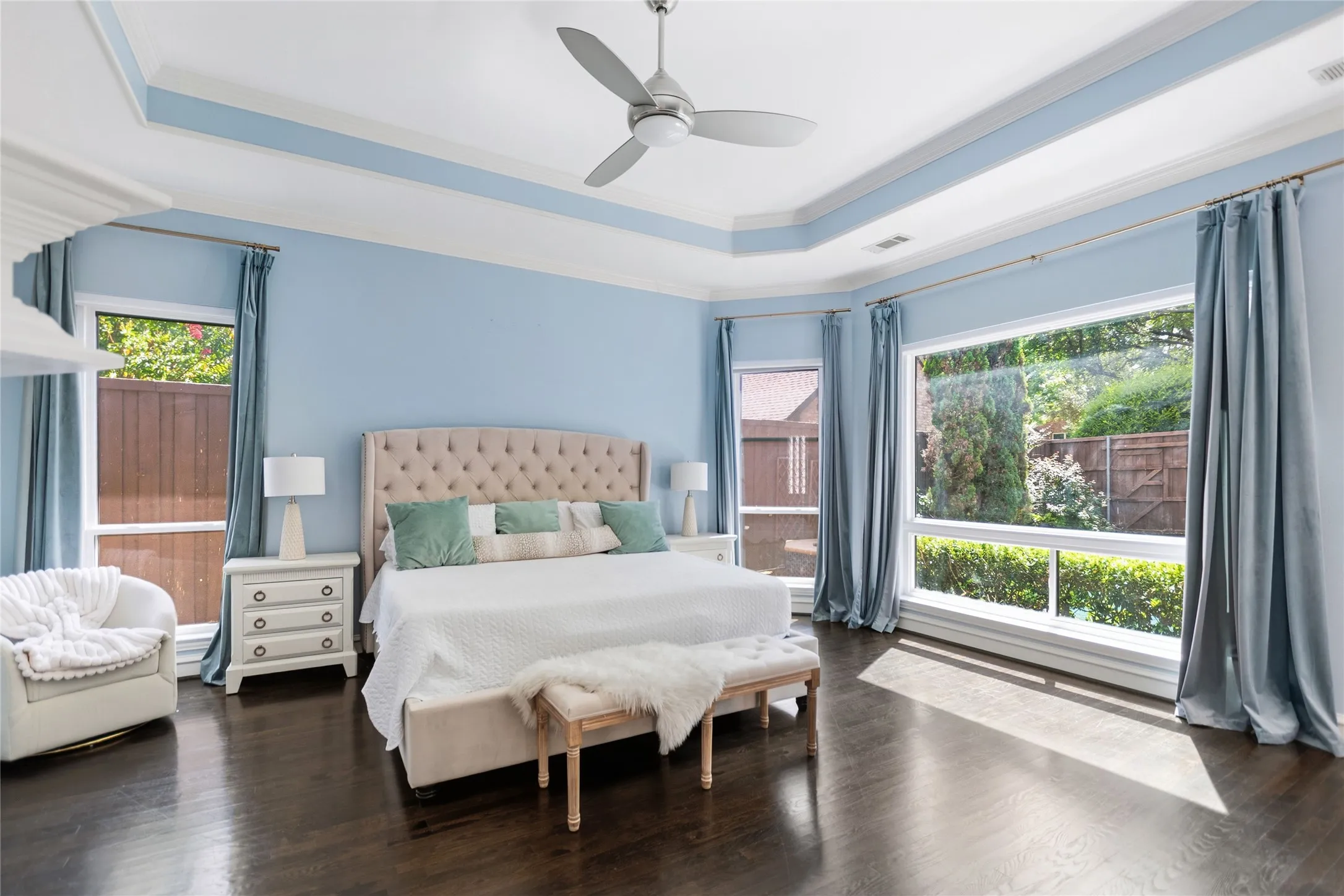 Spacious room featuring rich wood-finish flooring, a tray ceiling, and a ceiling fan
