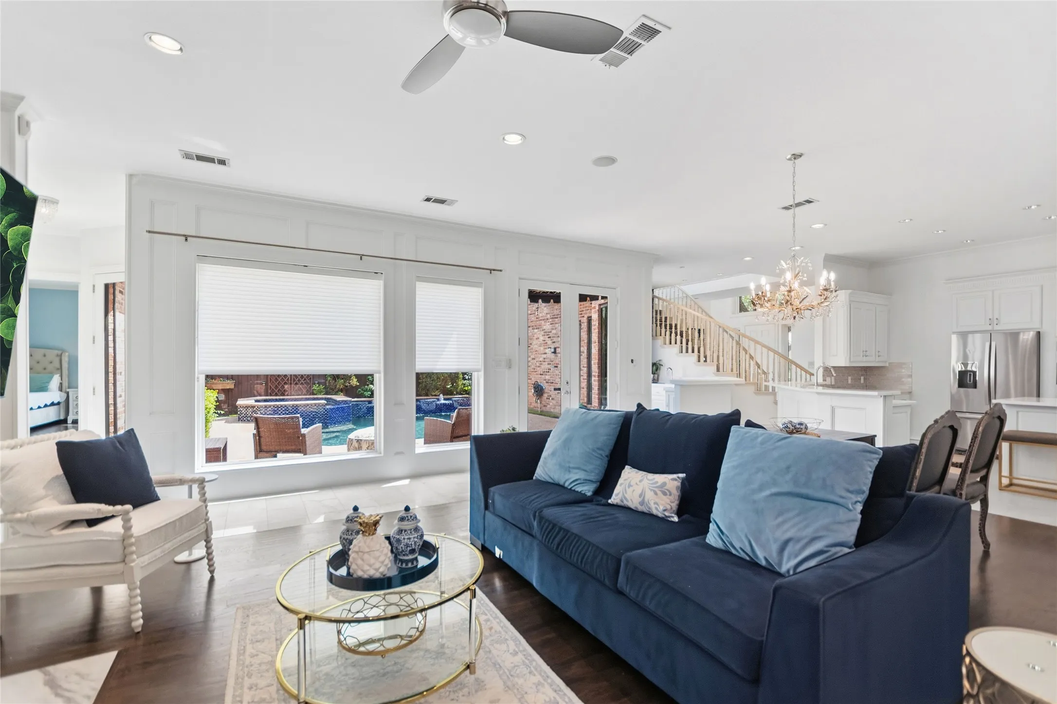 Spacious living area featuring large windows overlooking a pool, wood-finish flooring, a contemporary ceiling fan, recessed lighting, and a grand staircase with white balusters