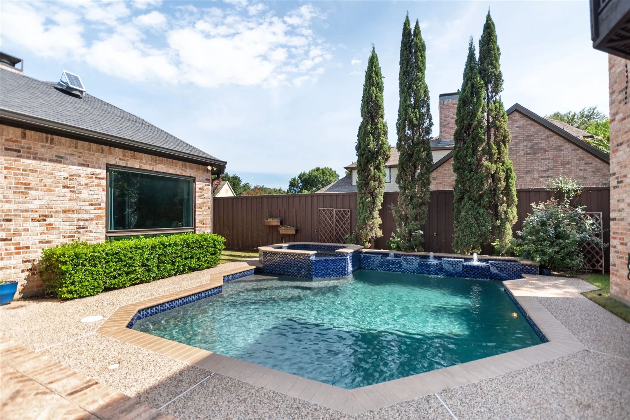 Swimming pool with integrated spa and water features, surrounded by exposed aggregate concrete decking