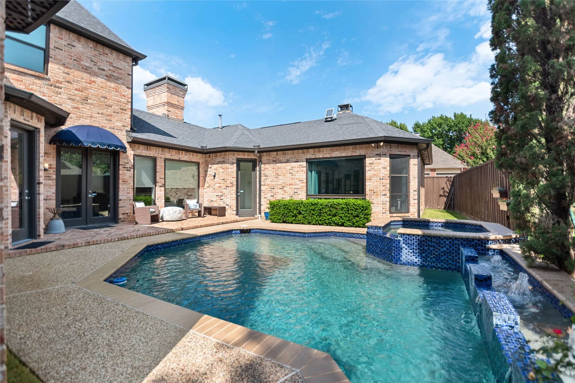 Brick-clad exterior with a blue awning, featuring a swimming pool, spa, and water feature