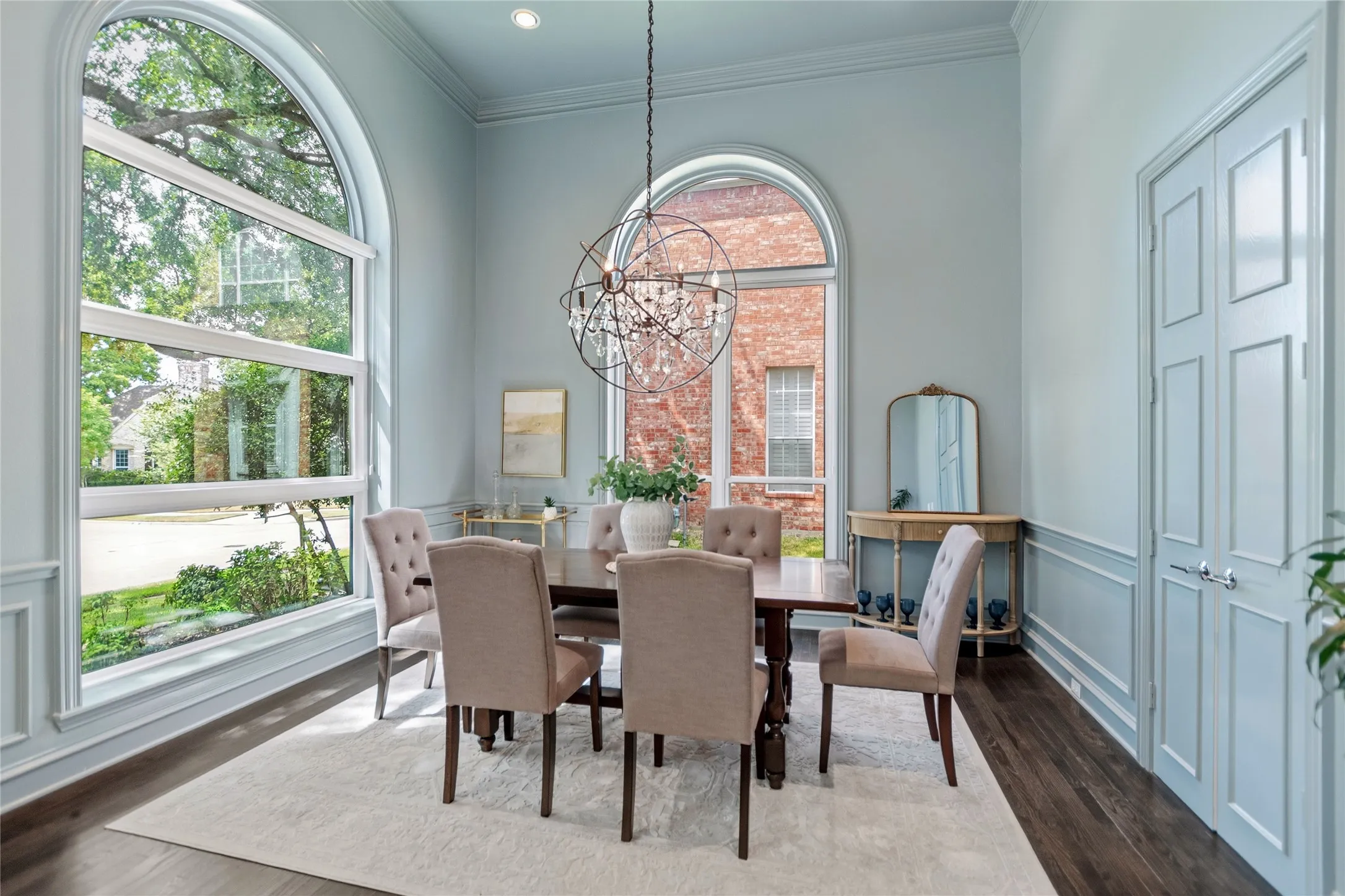 Dining area featuring dark wood-finish flooring, light blue paneled walls, and two arched floor-to-ceiling windows