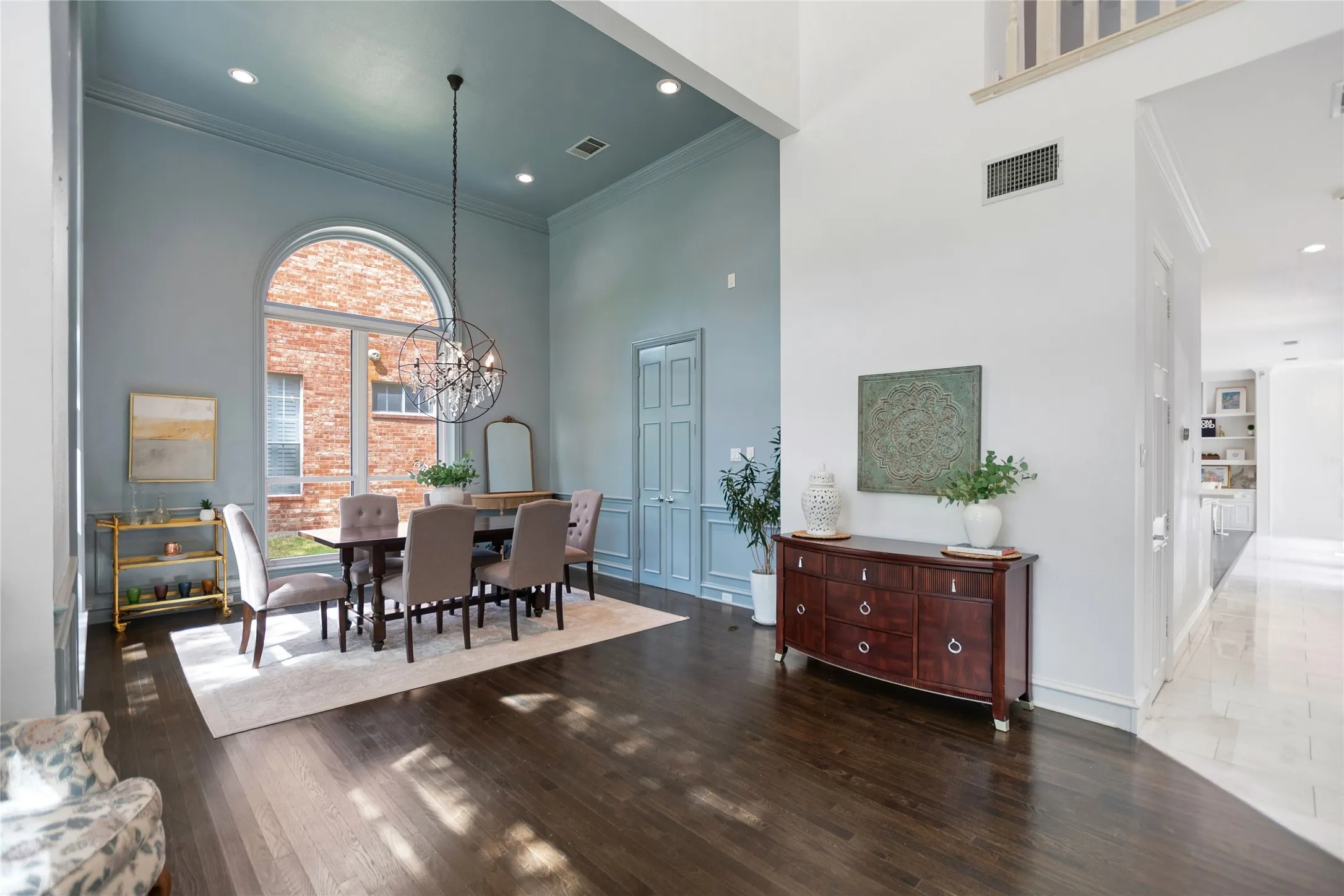 Formal dining area featuring a large arched window with white trim, wood-finish flooring, and recessed lighting