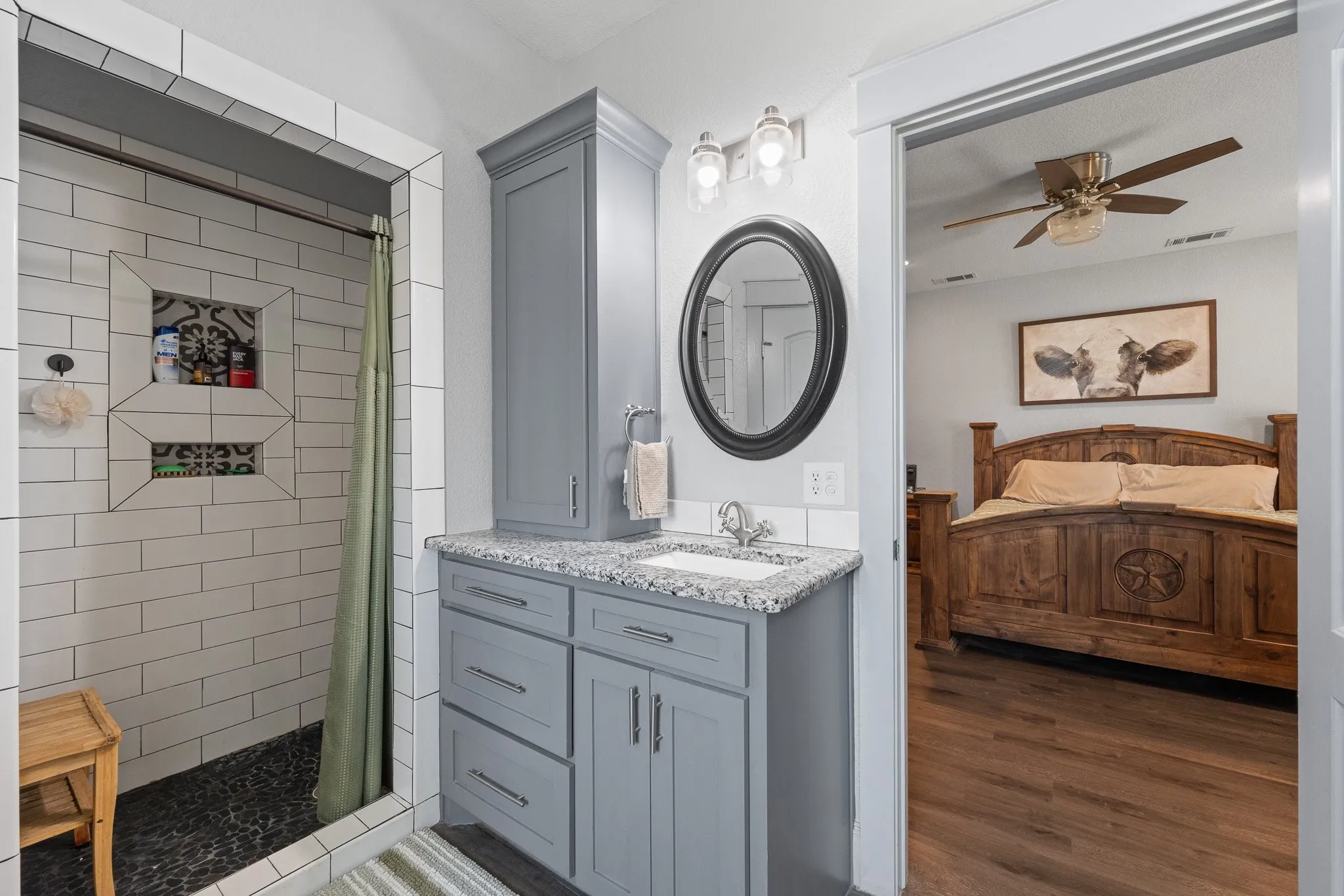 Bathroom vanity with gray cabinetry and speckled countertop, featuring a circular mirror and overhead lighting