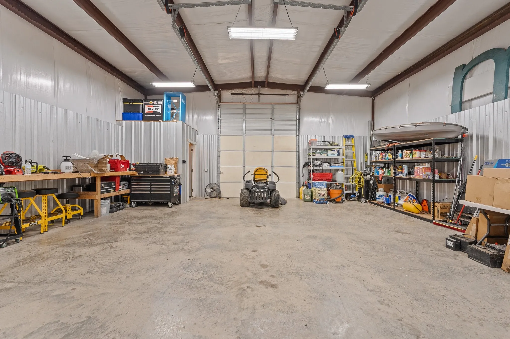 Spacious metal-sided building featuring exposed structural beams, concrete flooring, and an overhead door