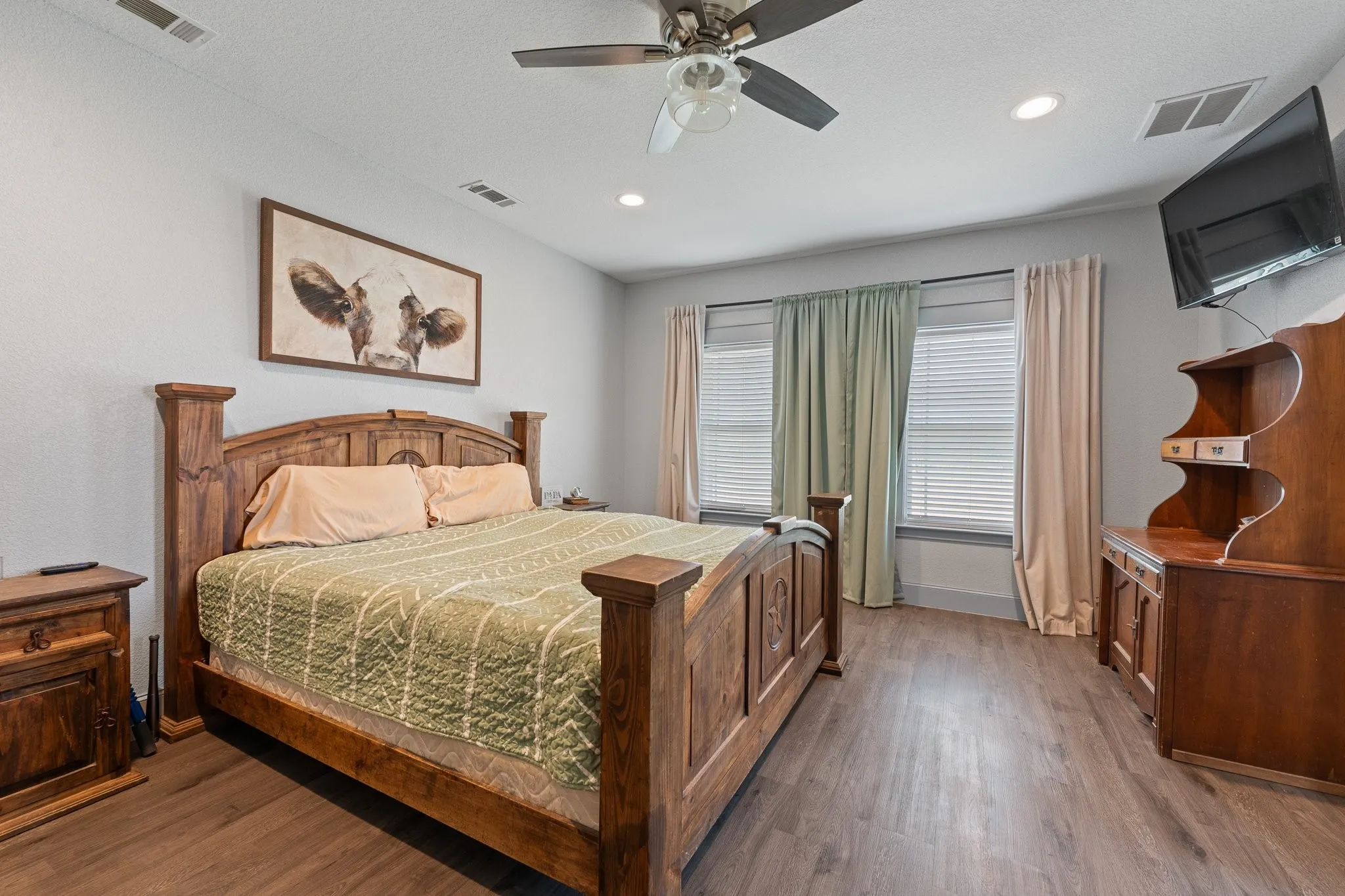 Spacious primary bedroom showcasing a wood-frame bed, warm wood-finish flooring, and recessed ceiling lighting