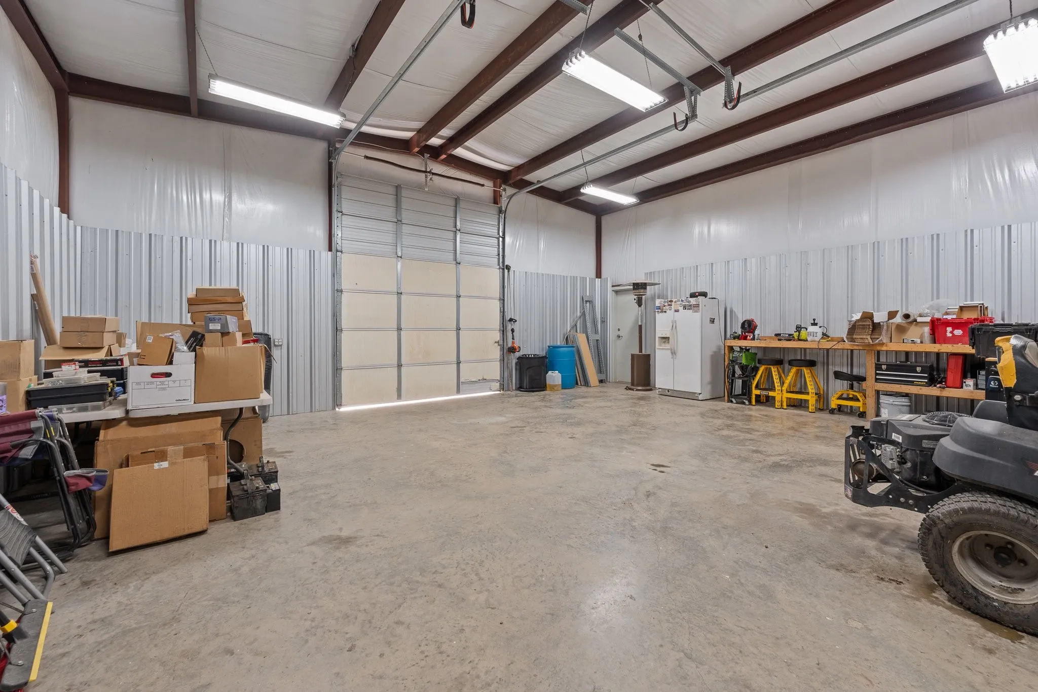 Spacious metal building featuring a large overhead door, concrete flooring, exposed steel beams, and strip lighting fixtures
