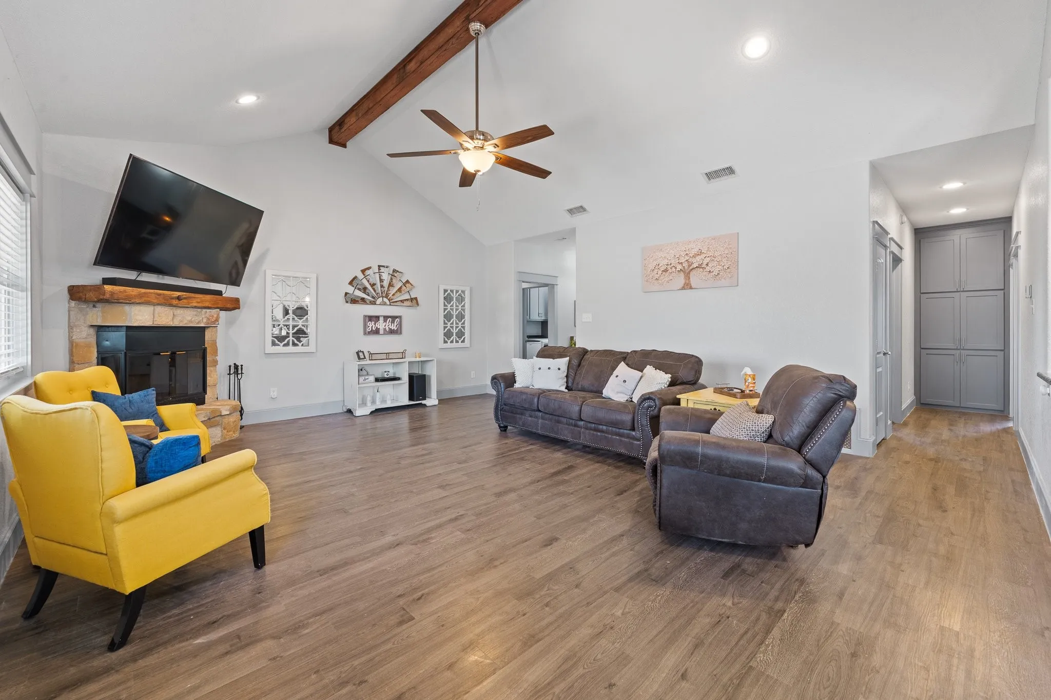 Spacious living area featuring a vaulted ceiling with exposed wood beams, wood-finish flooring, a stone fireplace with a wood mantel, and recessed lighting