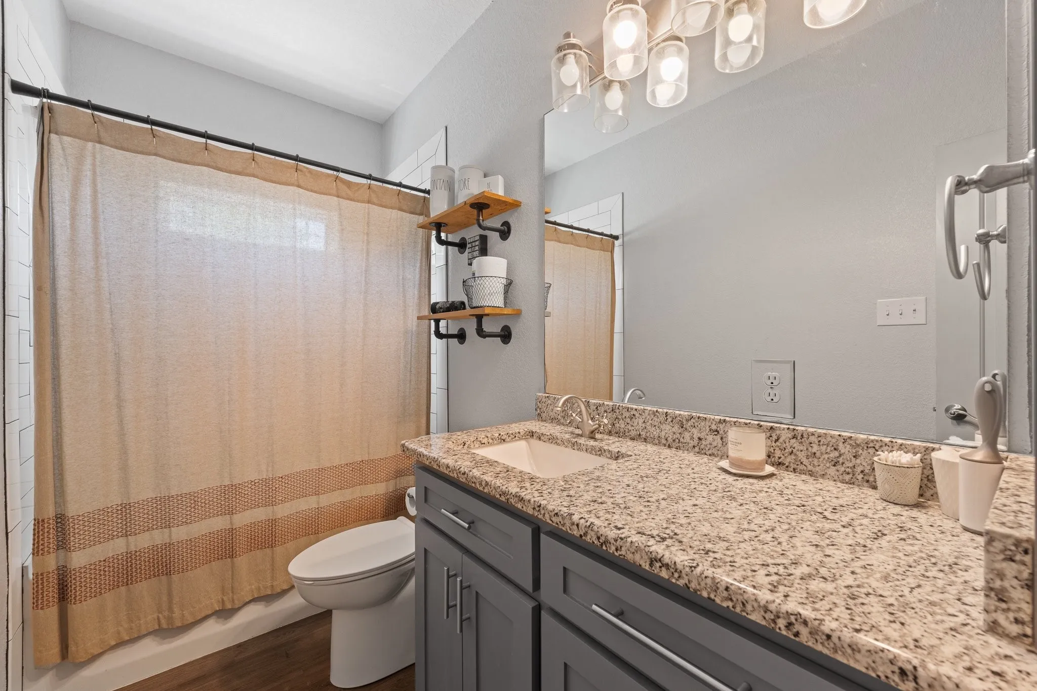 Bathroom featuring a spacious vanity with a speckled countertop, a large mirror, and an overhead light fixture with multiple bulbs