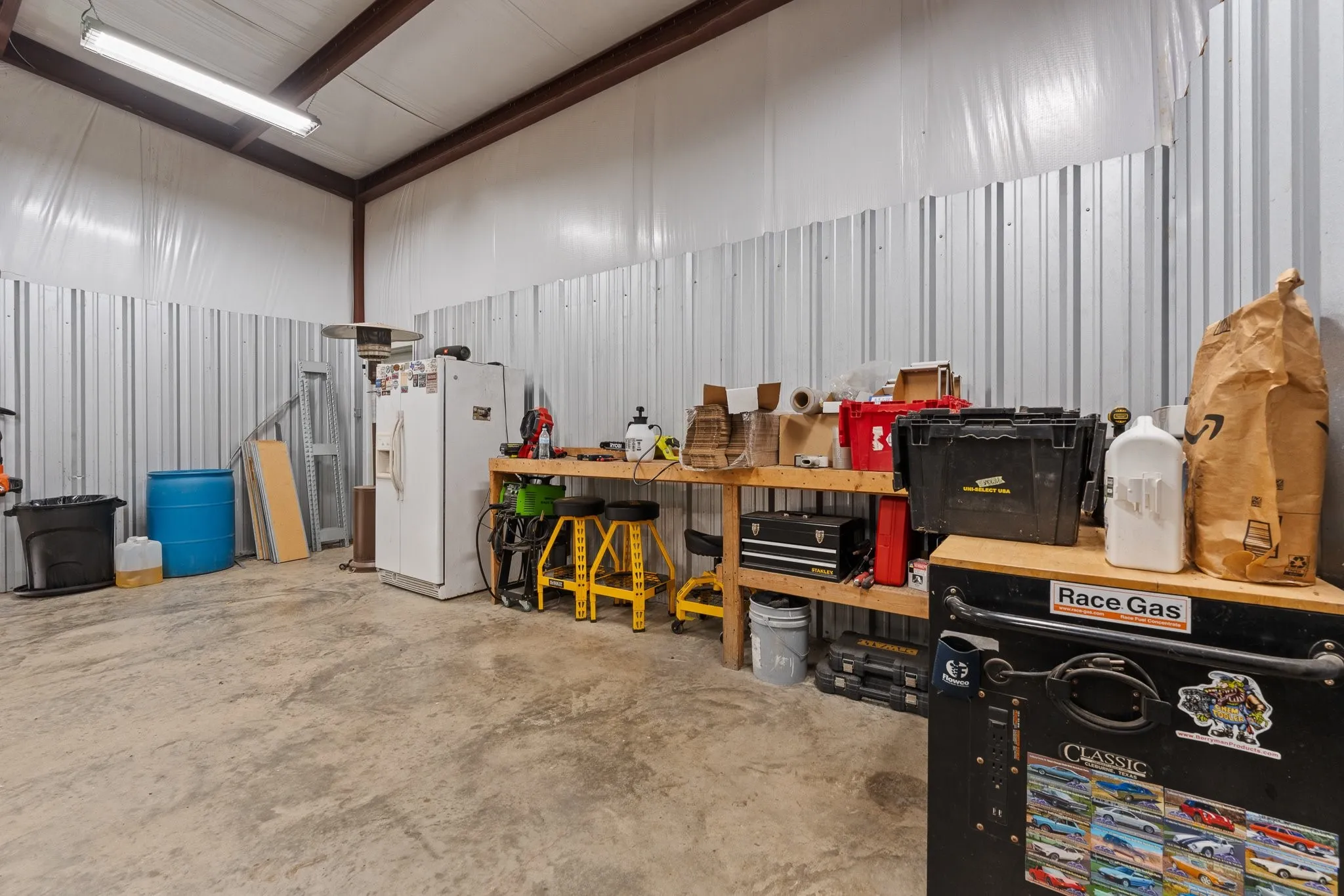Spacious utility building featuring concrete flooring, corrugated metal walls, exposed metal ceiling beams, and overhead fluorescent lighting