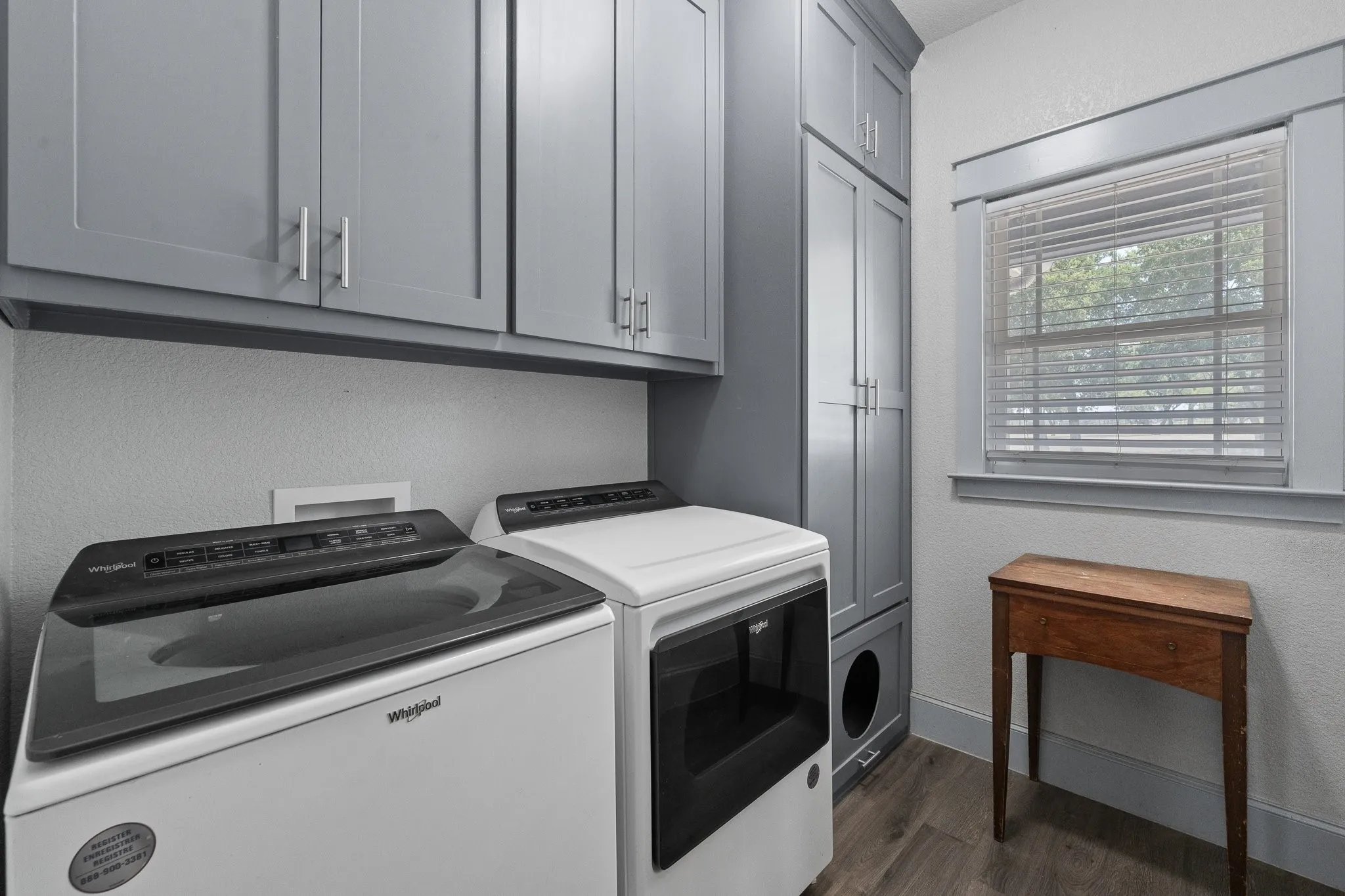Dedicated laundry space featuring extensive gray shaker-style cabinetry, wood-finish flooring, and a window with trim