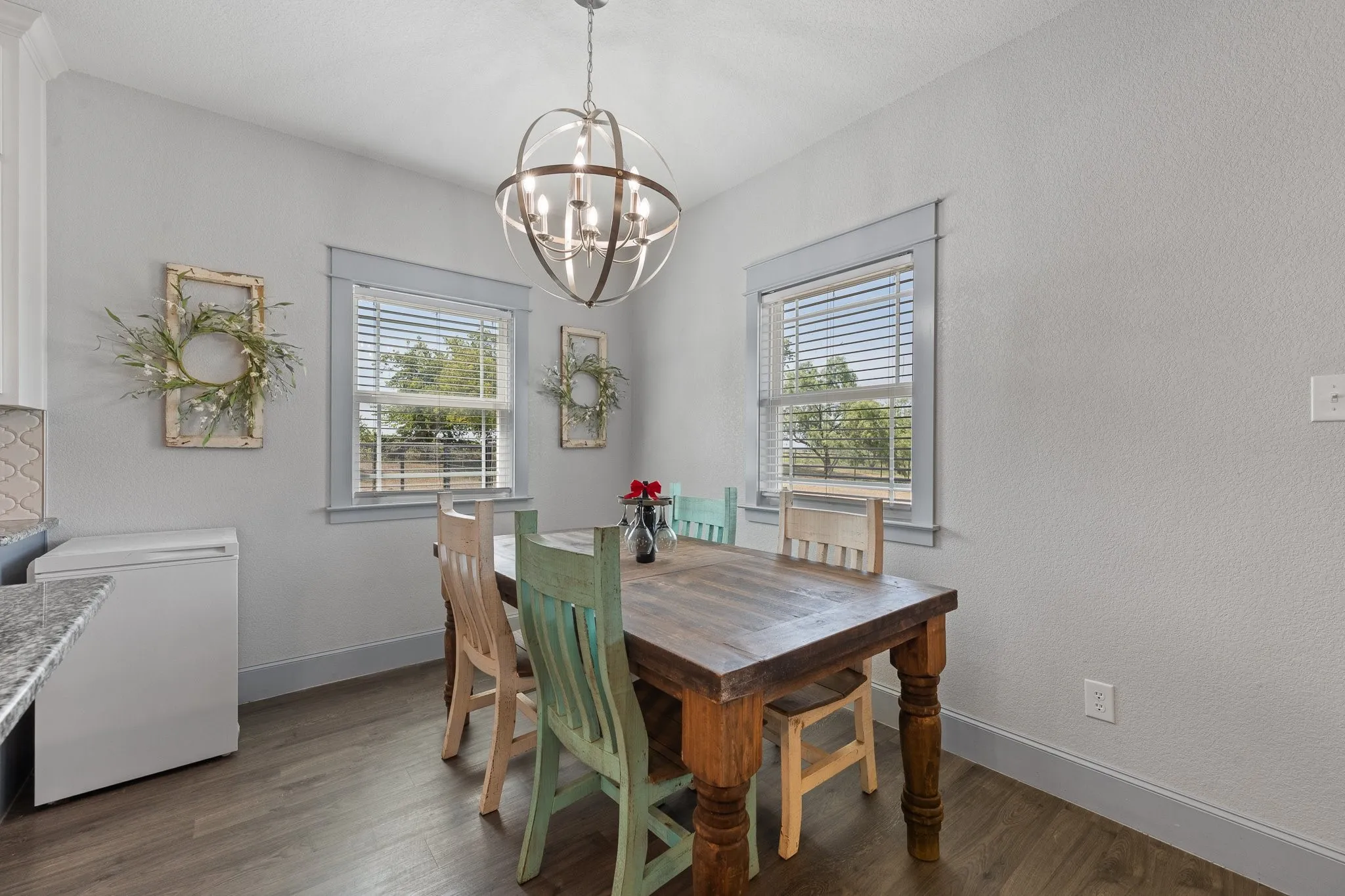 Dining area featuring wood-finish flooring, two windows with blinds, and a contemporary spherical chandelier