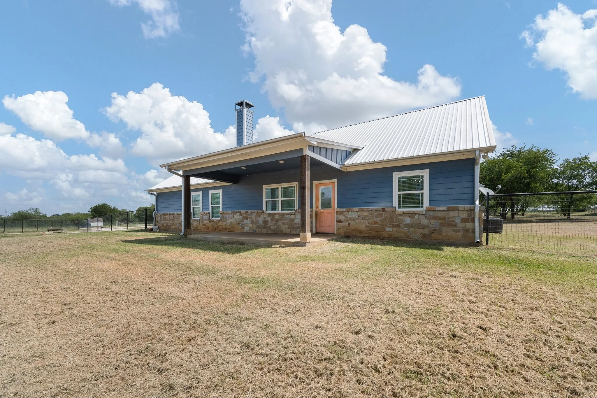 Rear exterior featuring a covered patio, blue siding, stone veneer accents, and a white metal roof