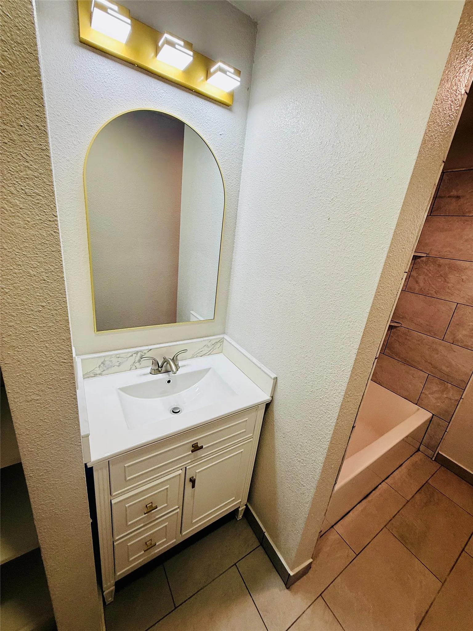 Bathroom vanity featuring a white cabinet with gold-tone hardware, a white countertop, and an integrated sink