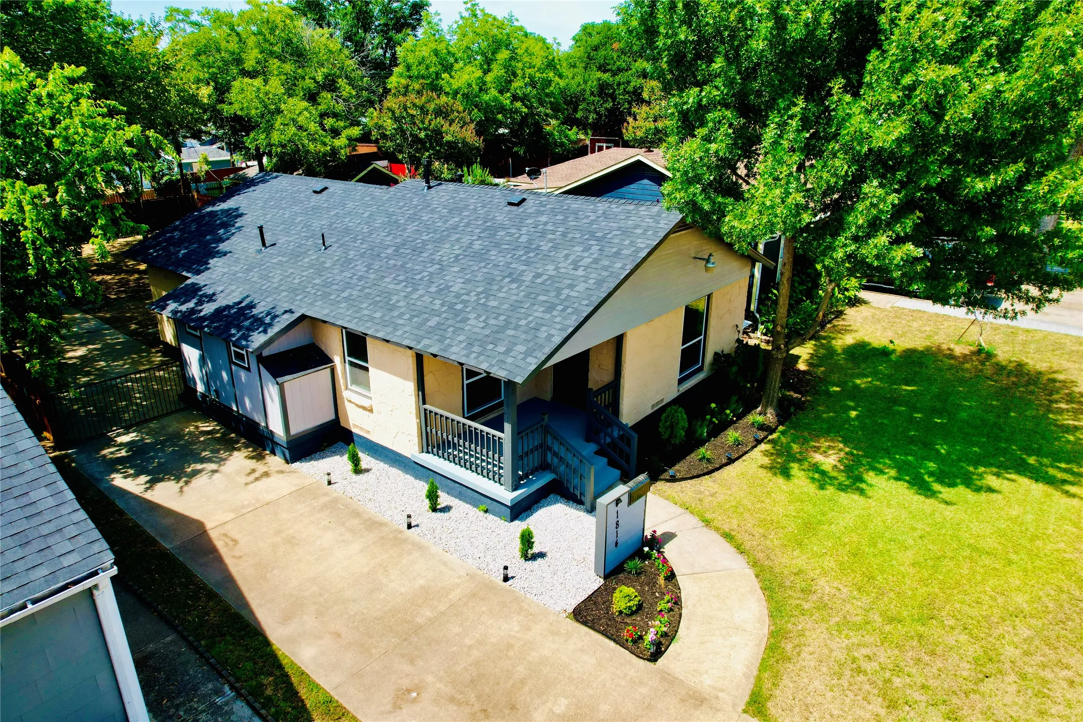 Exterior featuring a light-colored facade, dark shingle roof, covered front porch with dark railings, and a concrete driveway
