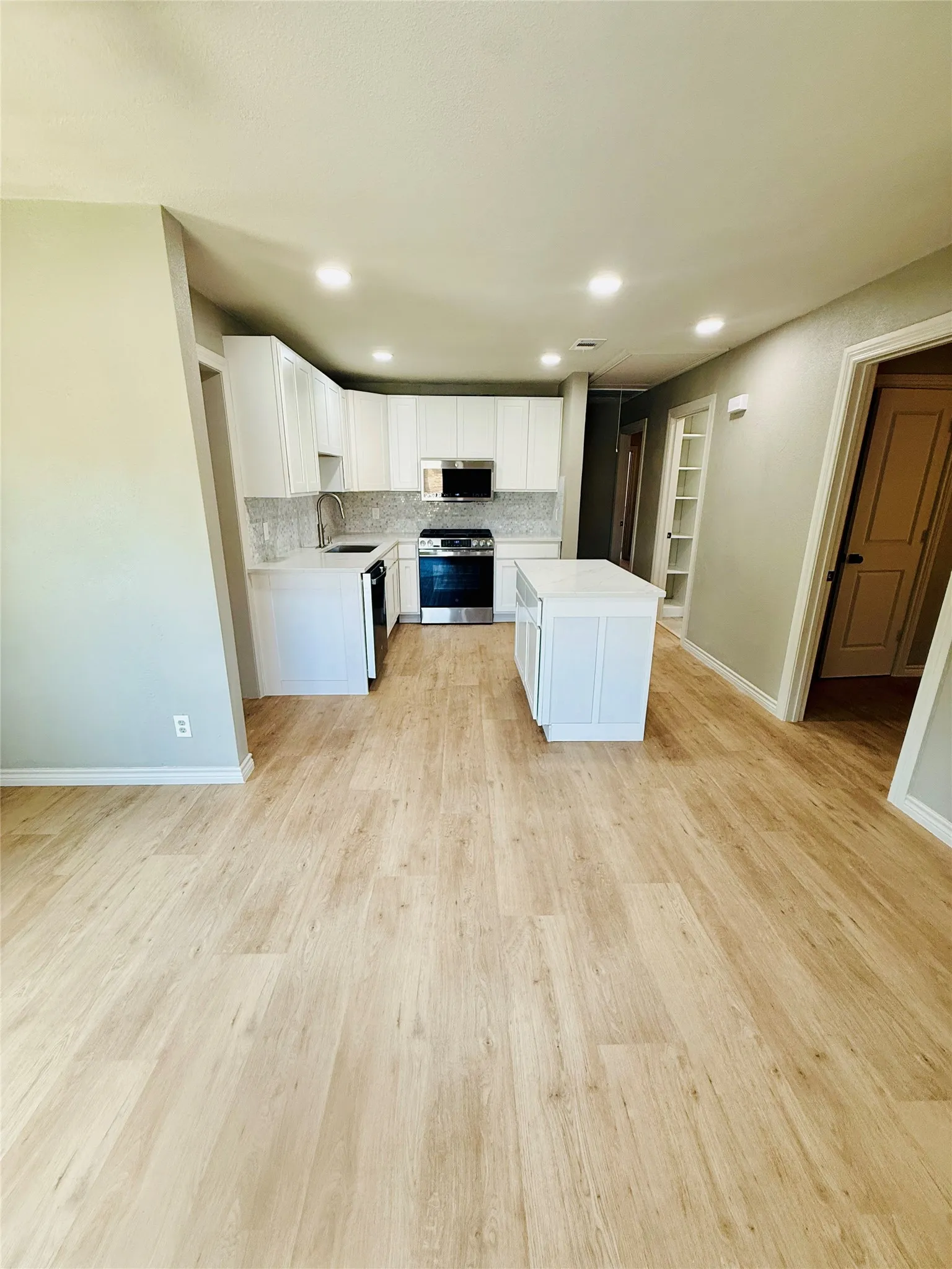 Open-concept kitchen featuring white cabinetry, stainless steel appliances, and a light-toned wood-finish flooring