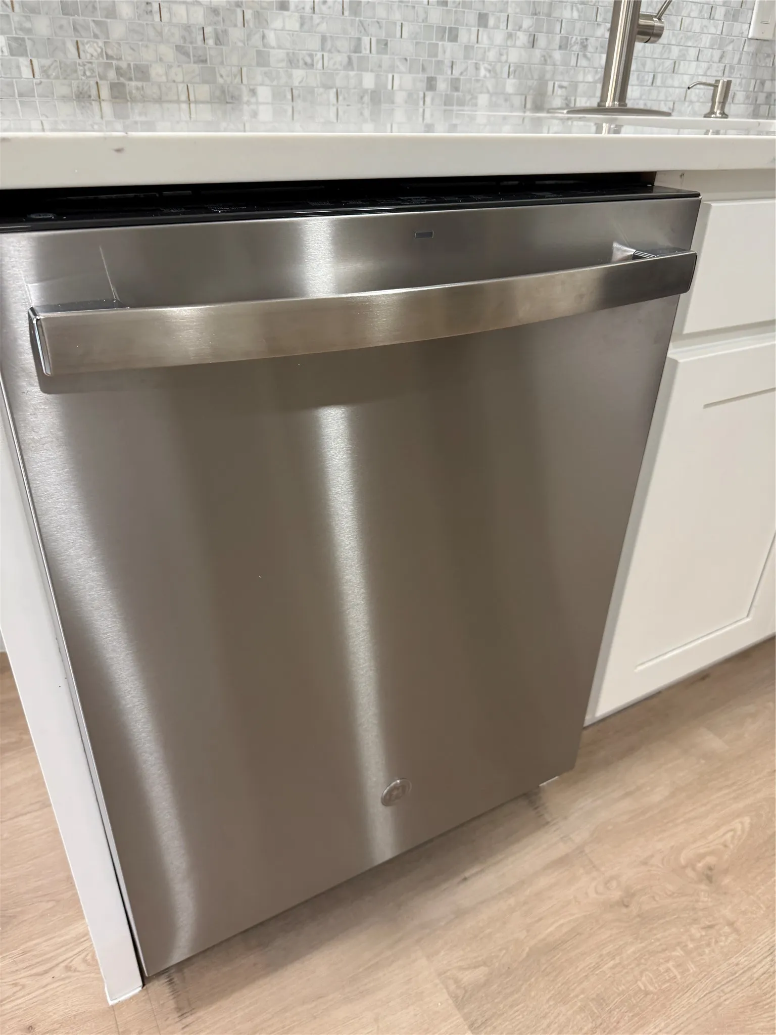 Stainless steel dishwasher integrated into white cabinetry with a light wood-finish floor