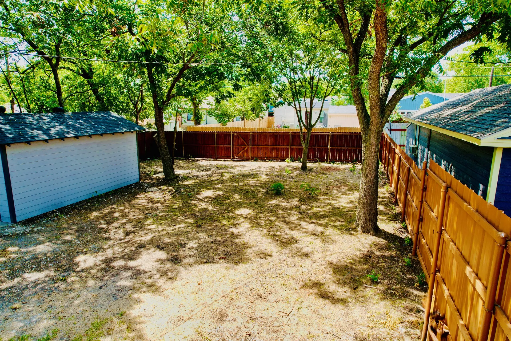 Spacious backyard featuring mature trees, a detached storage shed with shingle roofing, and privacy fencing