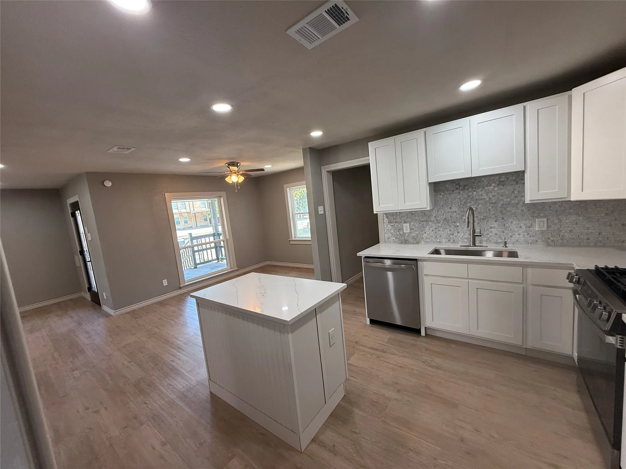 Modern kitchen featuring white shaker cabinetry, stainless steel appliances, a white tile backsplash, and light wood-finish flooring