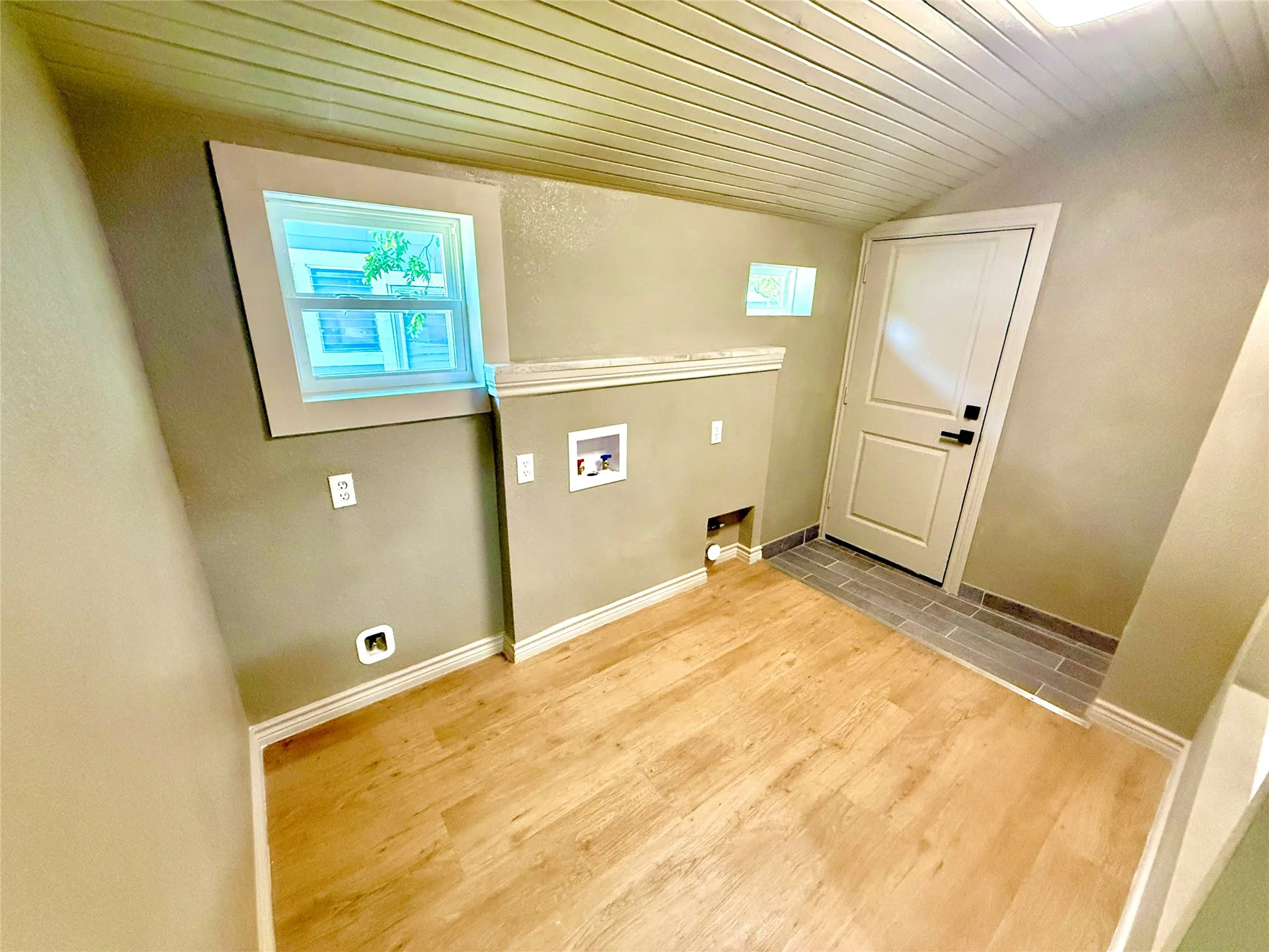 Utility space featuring wood-finish flooring, a white paneled door, and a horizontal slat ceiling