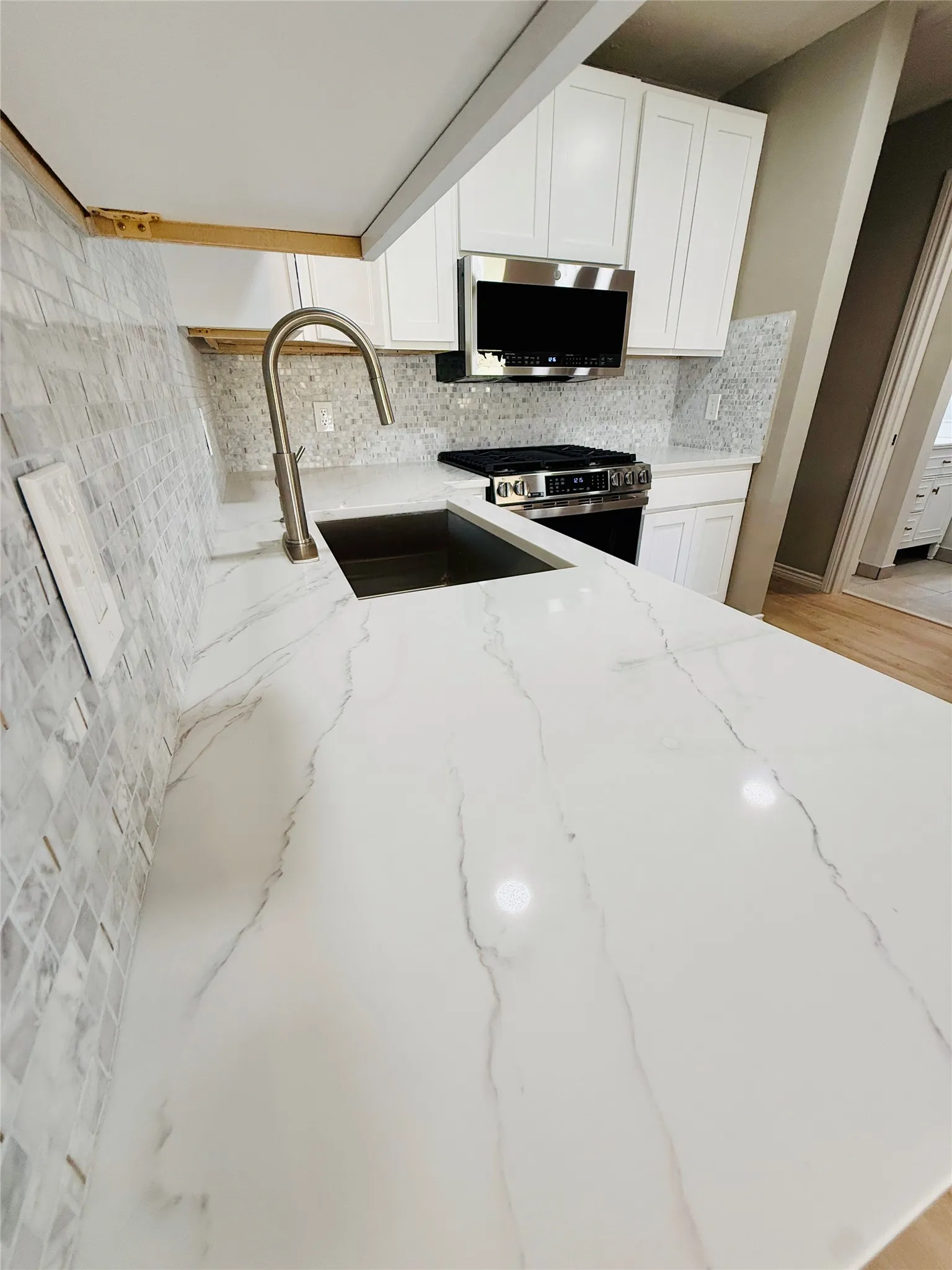 Kitchen featuring white cabinetry, a large white countertop with veining, and a stainless steel sink with a gooseneck faucet
