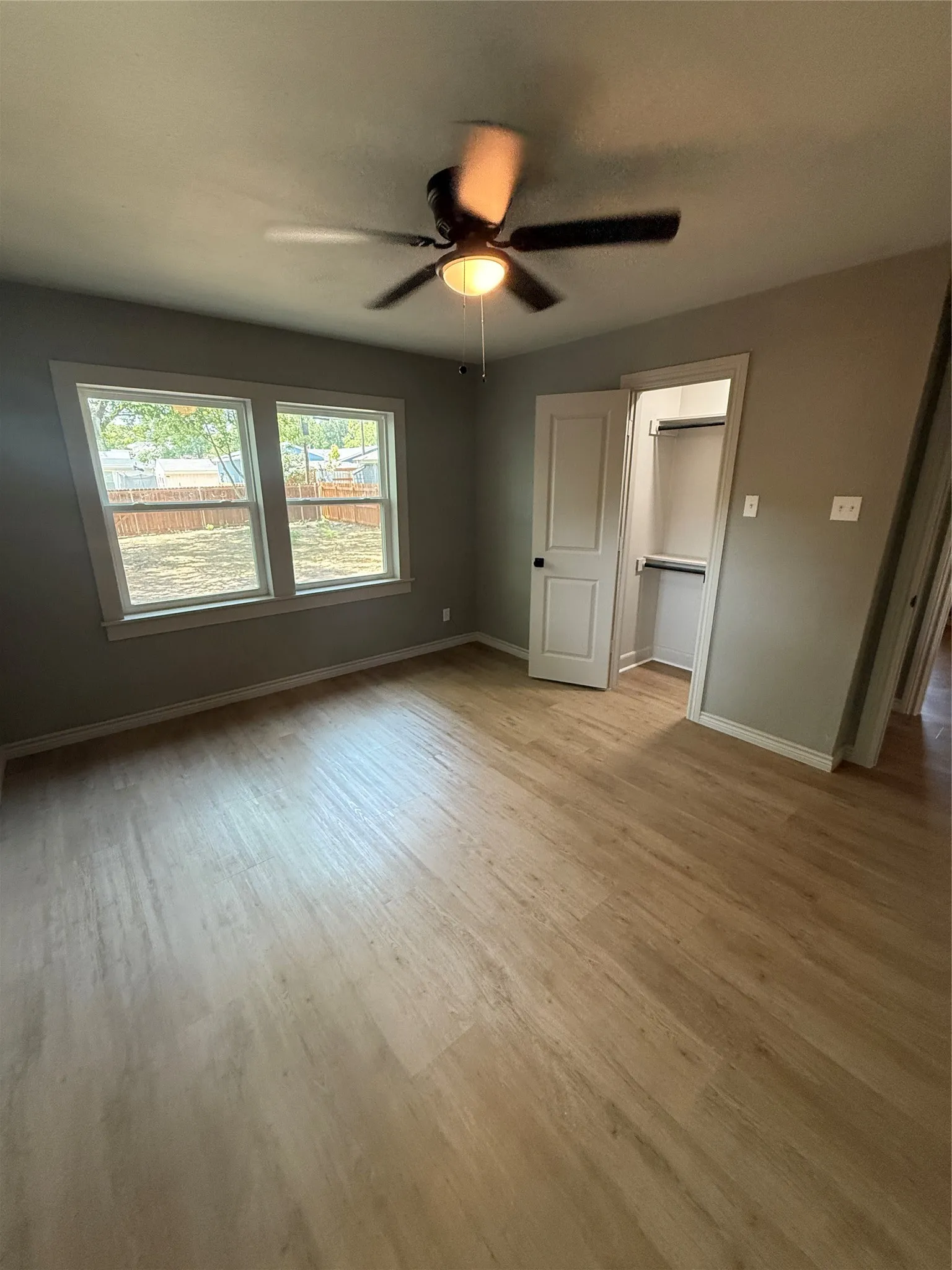 Bedroom featuring wood-finish flooring, two large windows, a ceiling fan with integrated lighting, a closet with shelving, and a neutral wall color