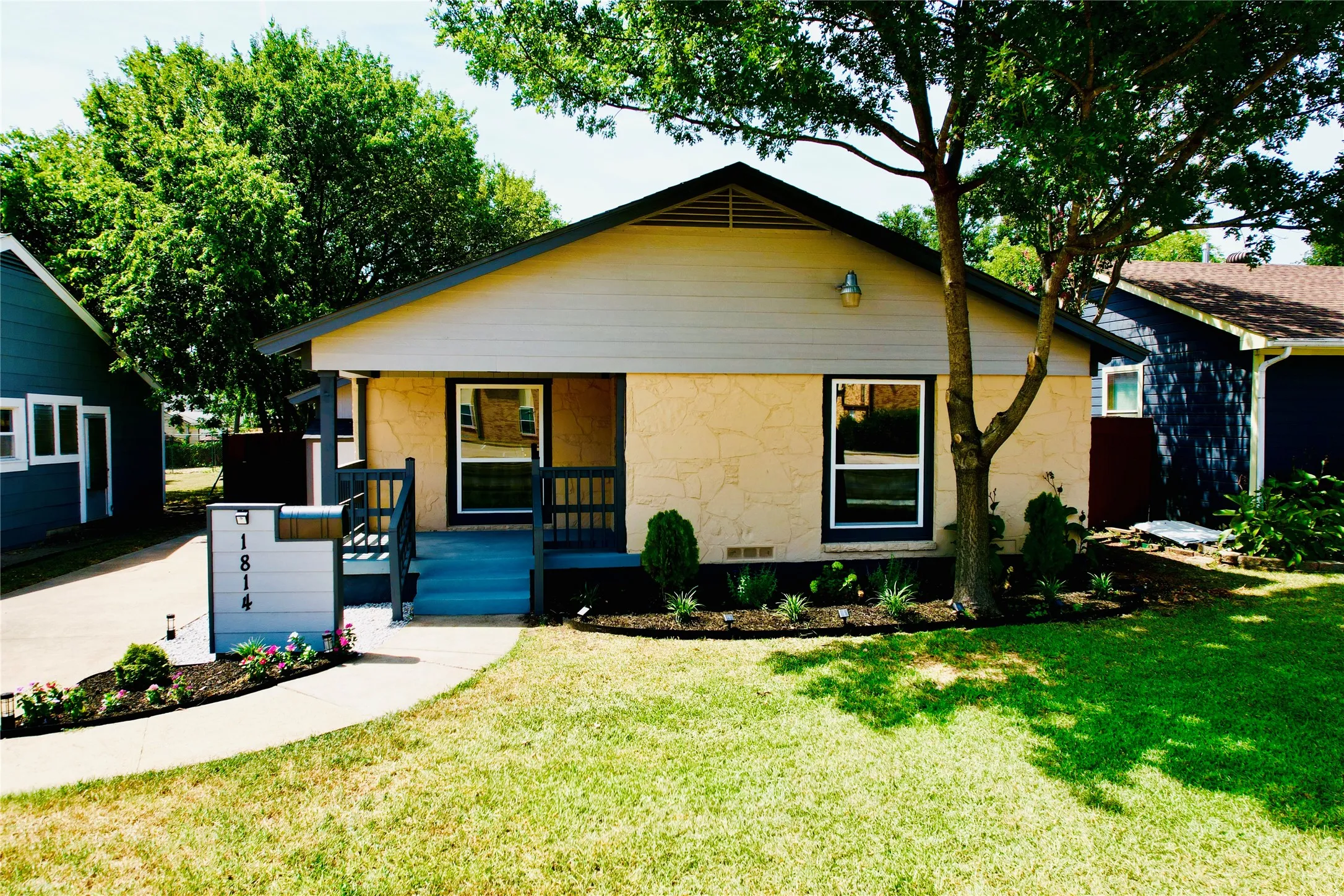 Single-story residence featuring a combination siding and stone facade, a covered front entry with blue steps, a manicured lawn, and a mature tree