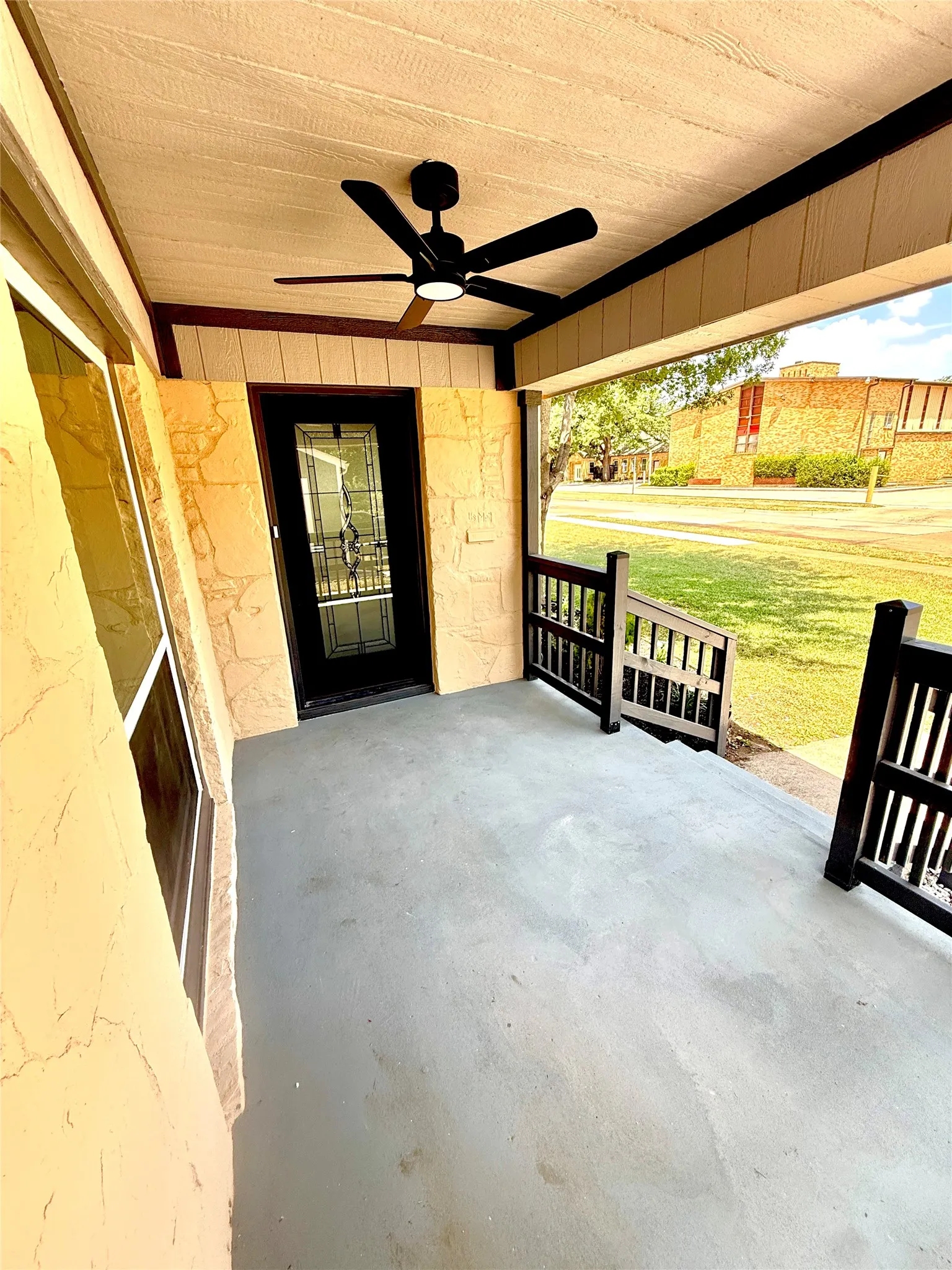 Covered front porch featuring a dark grey floor, textured ceiling, and a modern black ceiling fan with integrated lighting