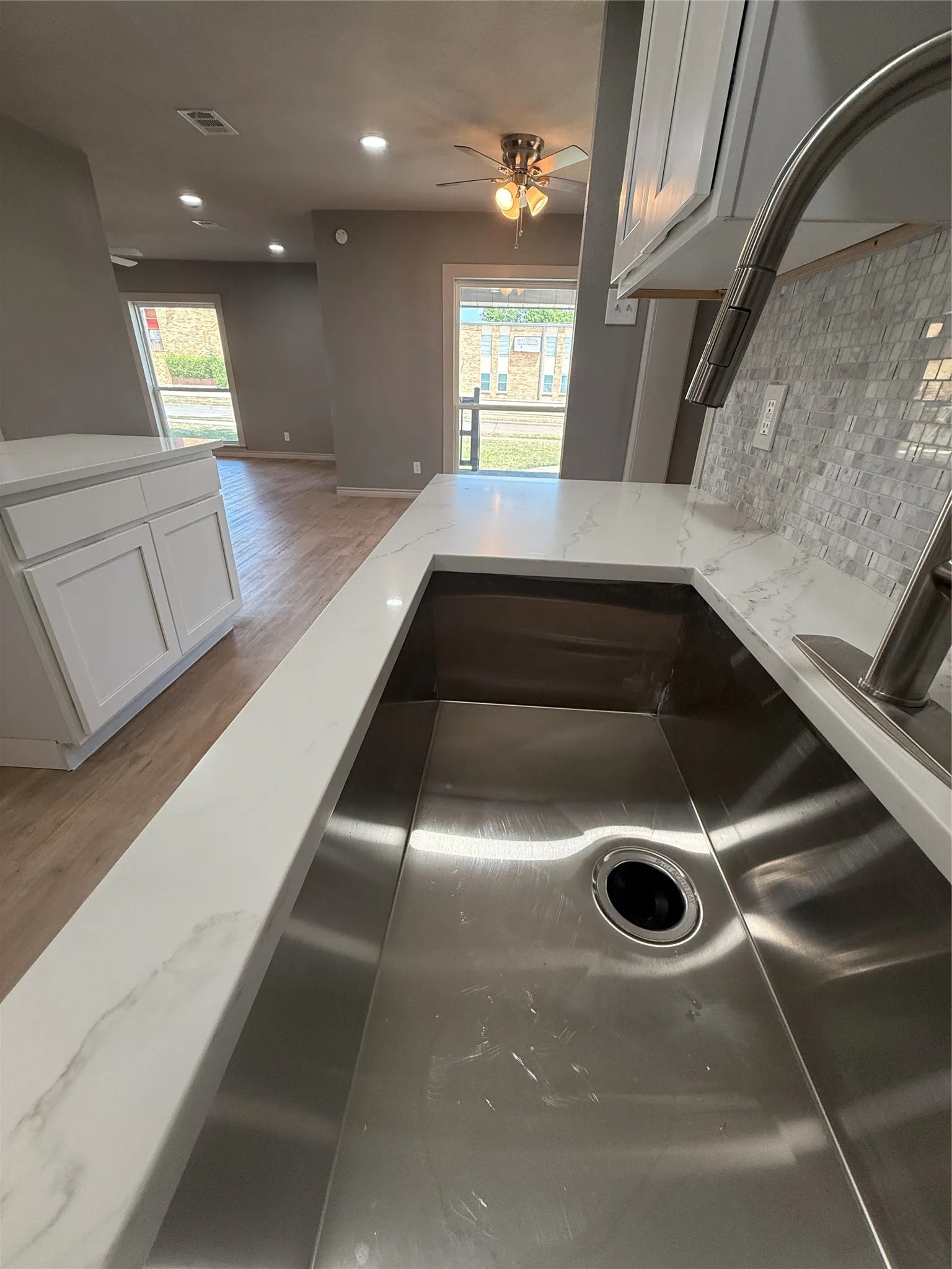 Kitchen featuring an undermount stainless steel sink, a pull-down faucet, a mosaic tile backsplash, and white cabinetry, complemented by a ceiling fan with integrated lighting