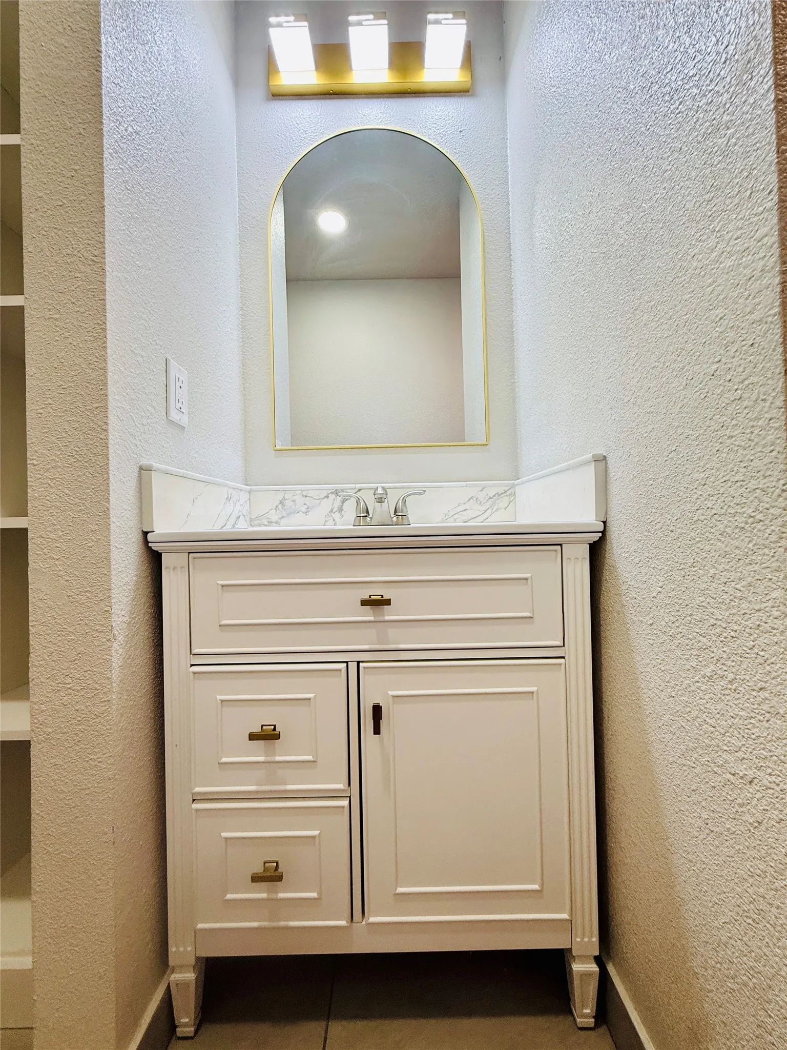 Vanity featuring a white paneled cabinet, brass hardware, and a white countertop with gray veining