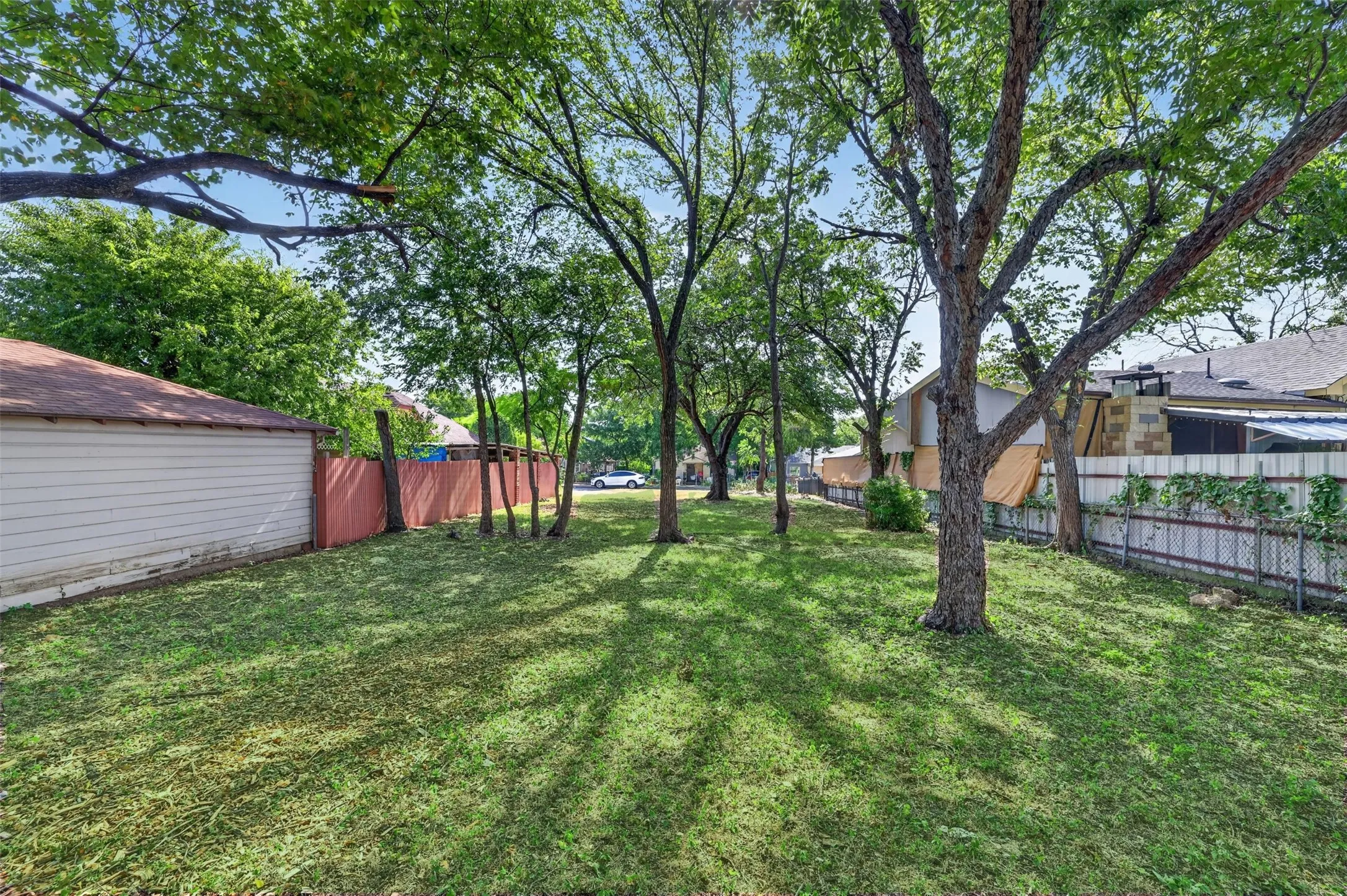 Expansive backyard featuring mature trees providing ample shade, a manicured lawn, and perimeter fencing