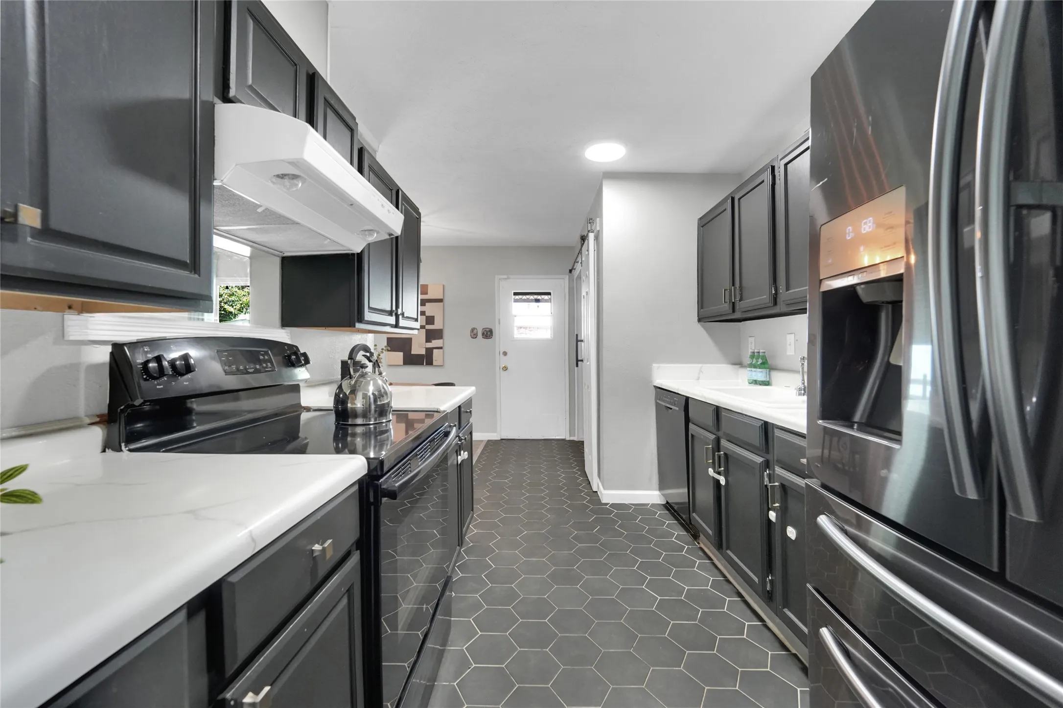 Galley kitchen featuring matte black cabinetry, stainless steel appliances, white countertops, and hexagon tile flooring