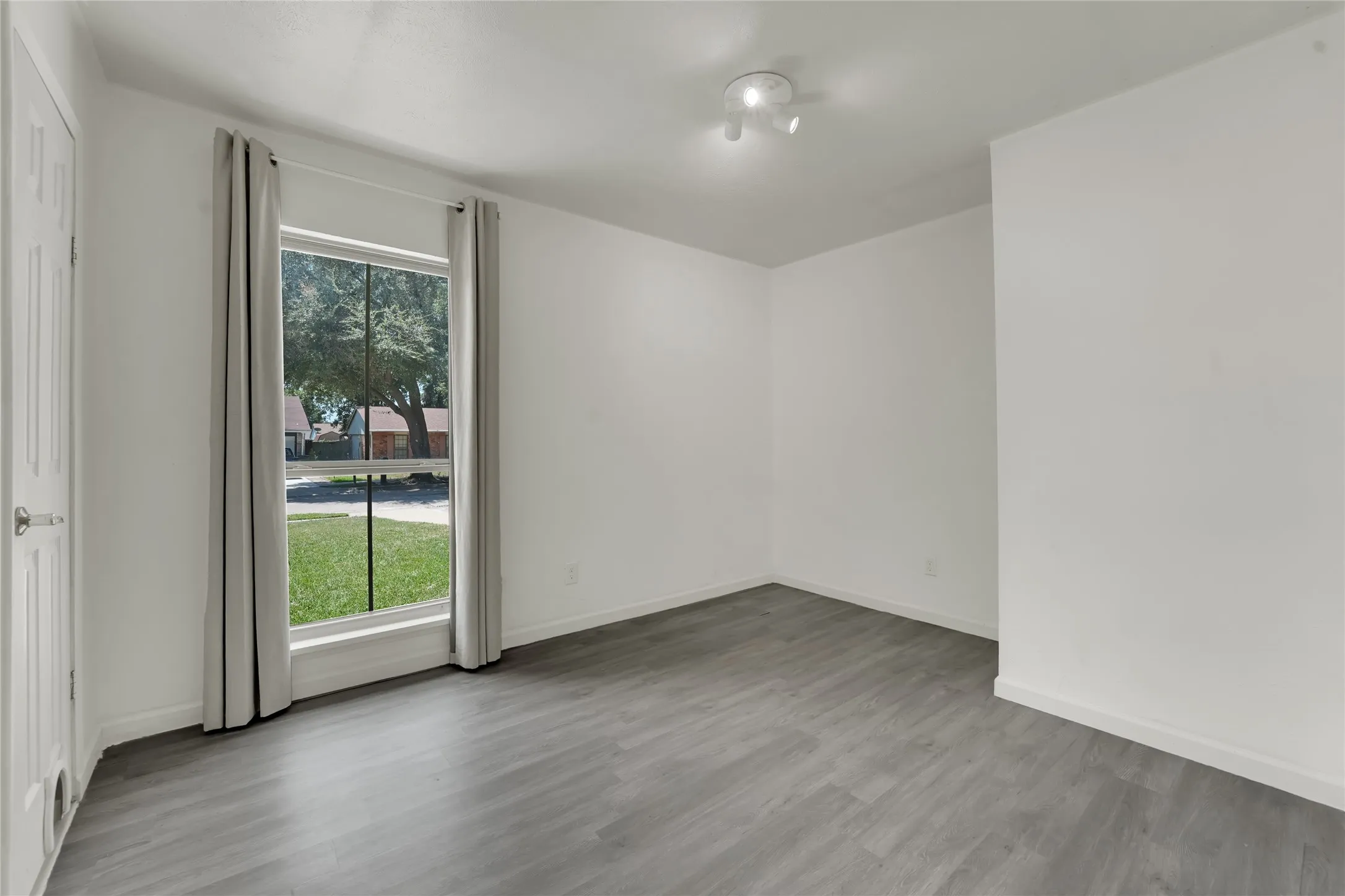 Spacious room with light gray wood-finish flooring, white walls, and a large window