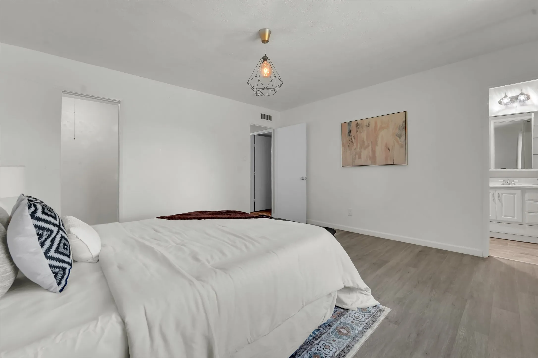 Expansive room with light wood-finish flooring, white walls, and a geometric pendant light fixture