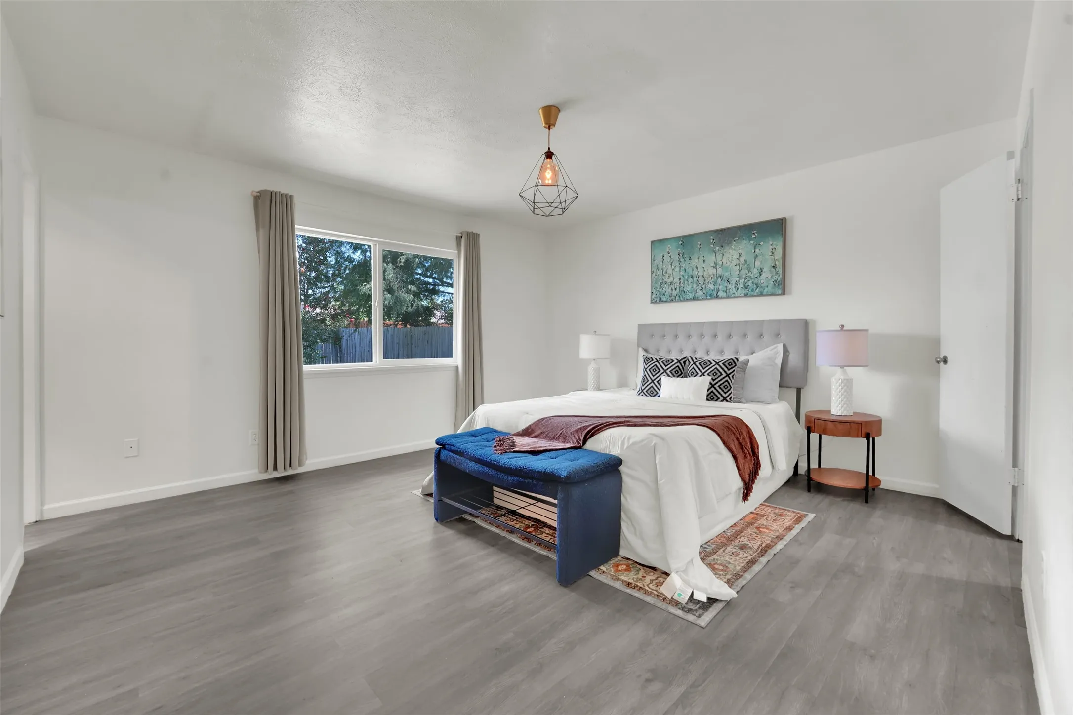 Spacious room featuring wood-finish flooring, white walls, and a large window